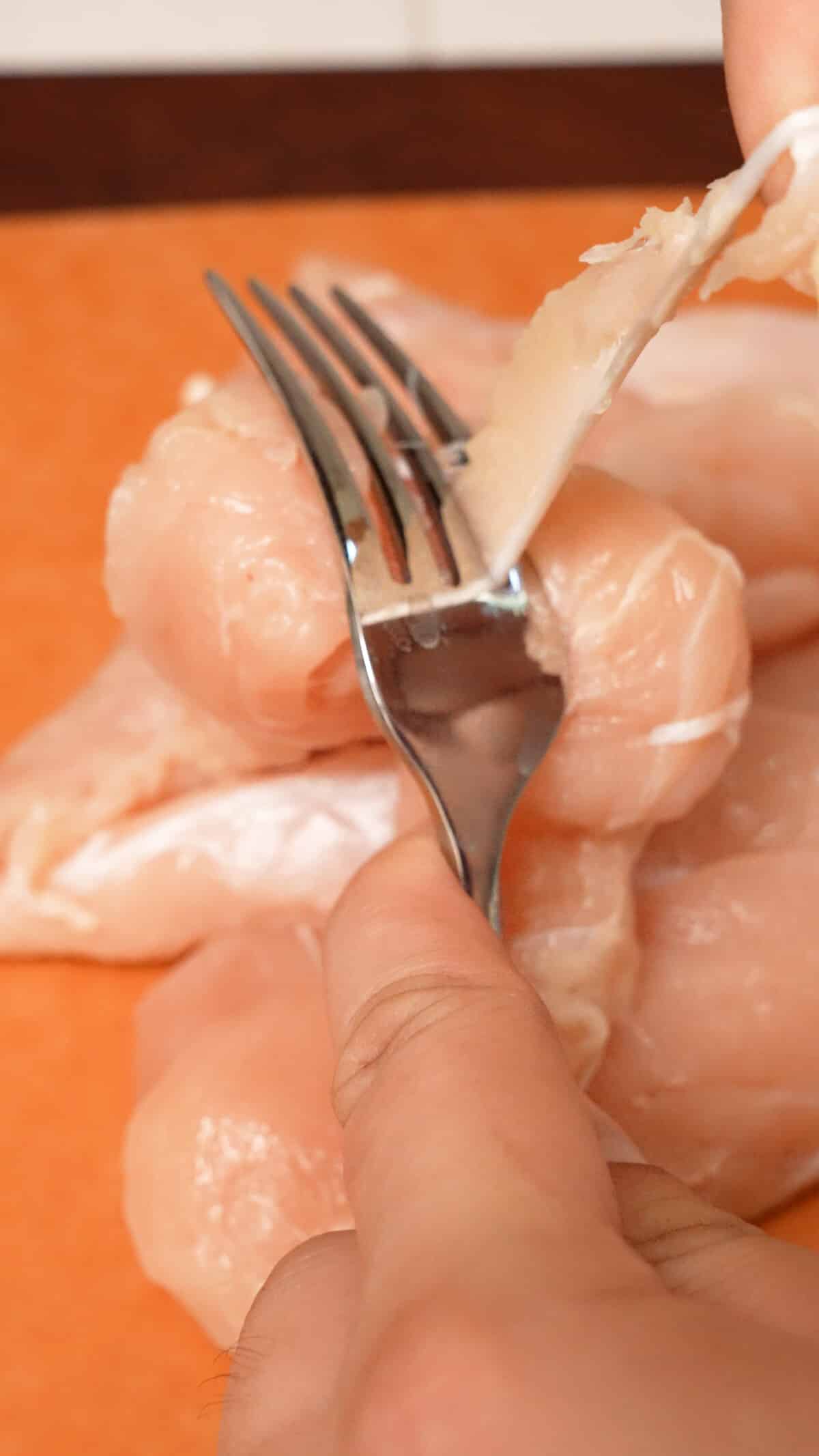 A hand pulling a chicken tender tendon through a fork.