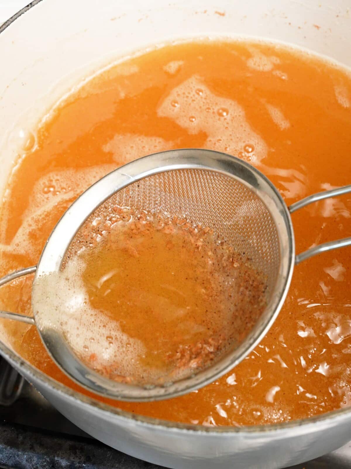 A mesh strainer straining loose bits of batter from frying oil.