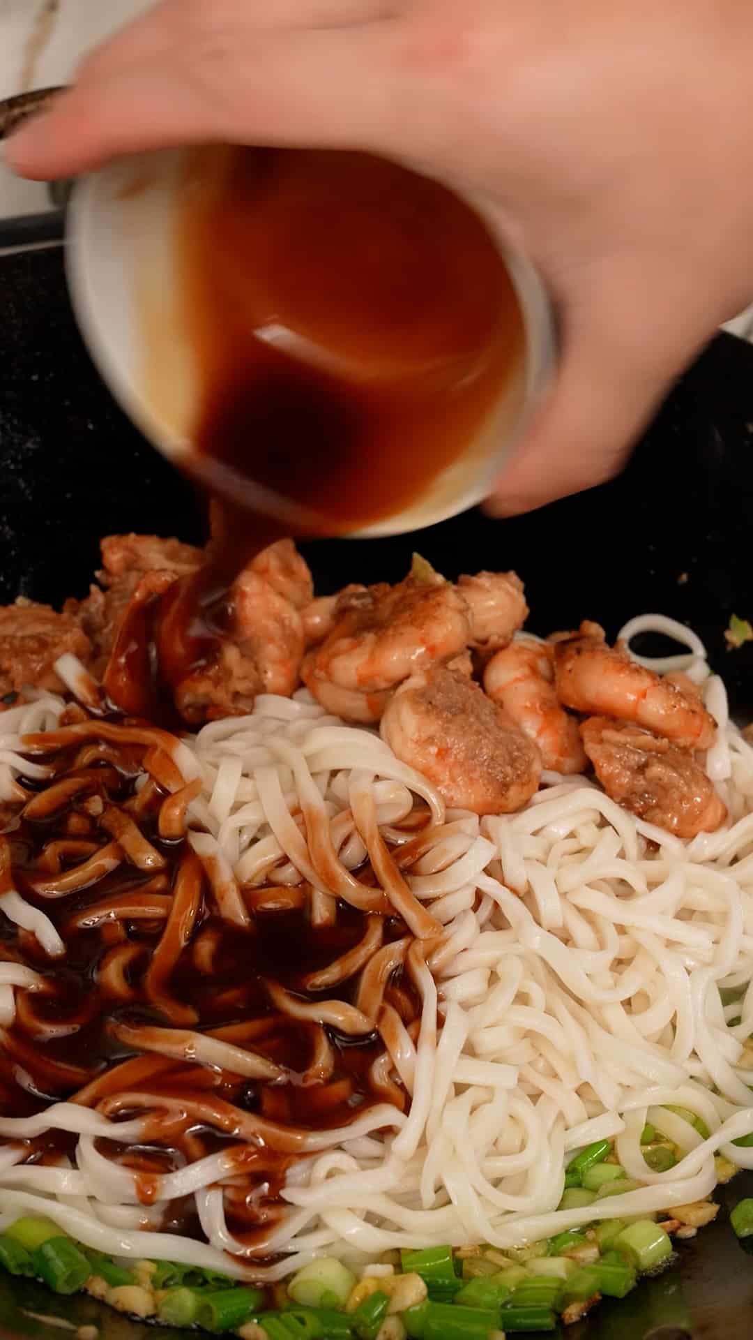 Adding the sauce to the noodles and shrimp in a wok.