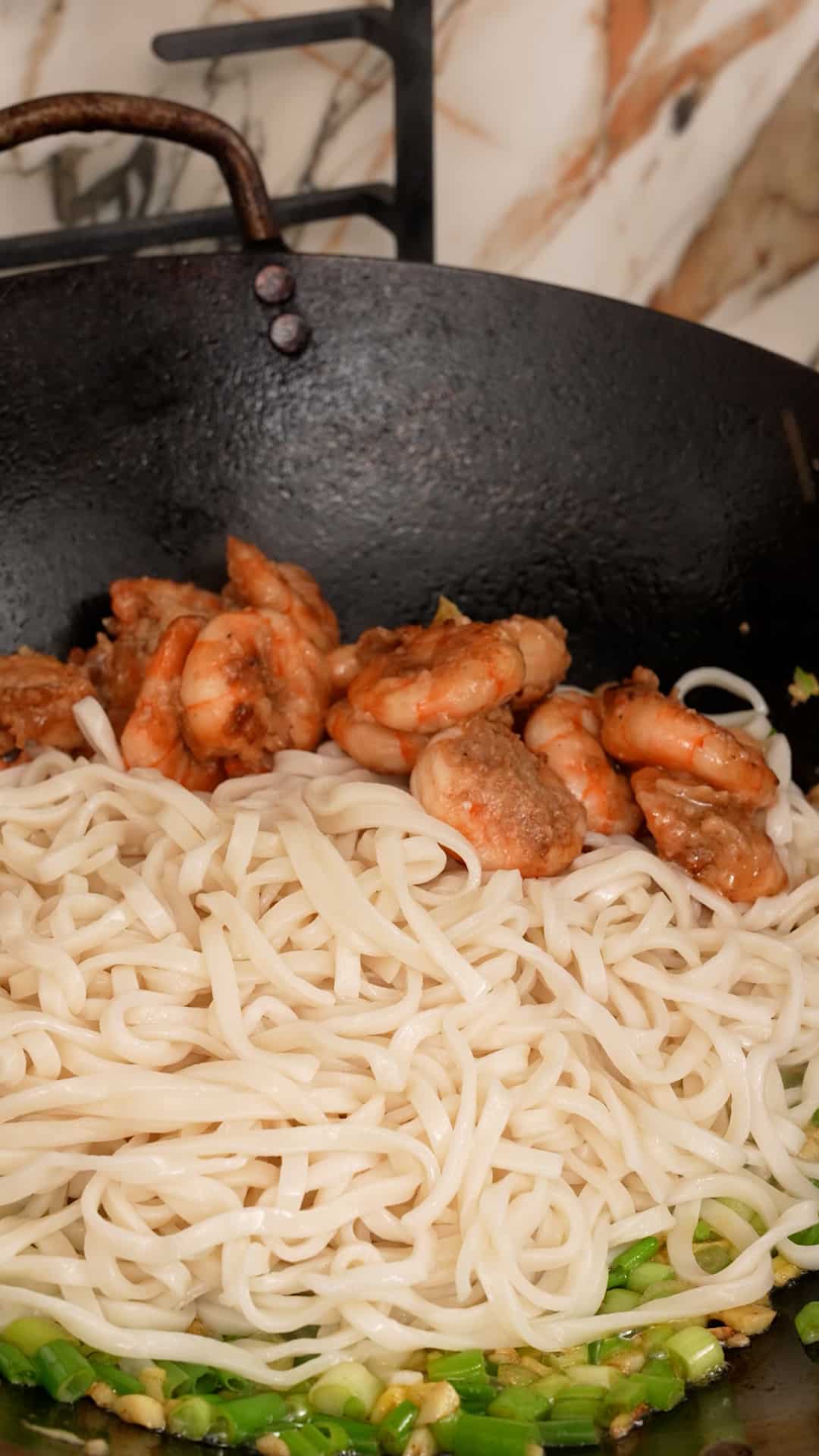 Adding noodles and shrimp back to the wok with the scallions and garlic.