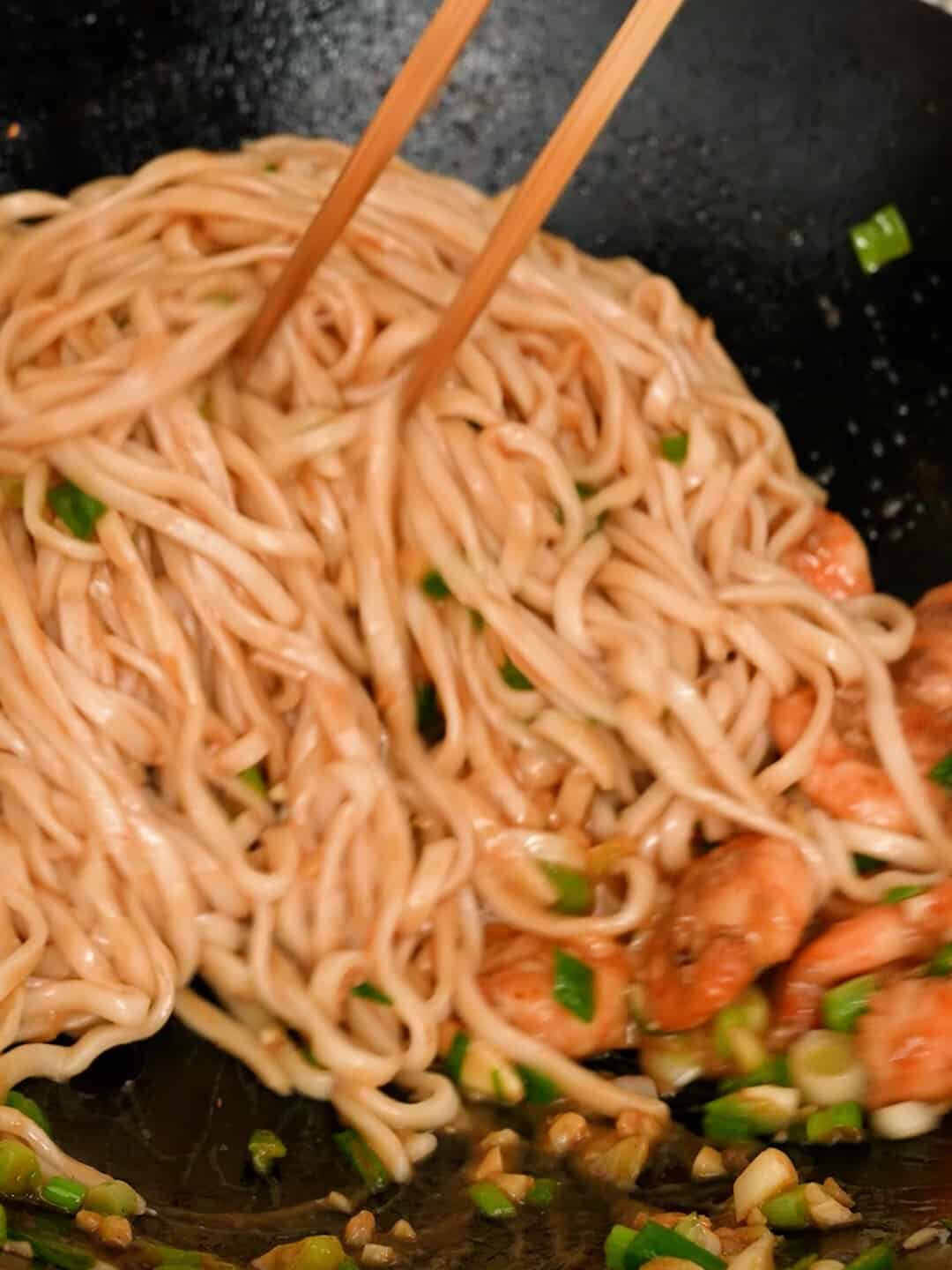 Mixing the noodles with shrimp in a wok.