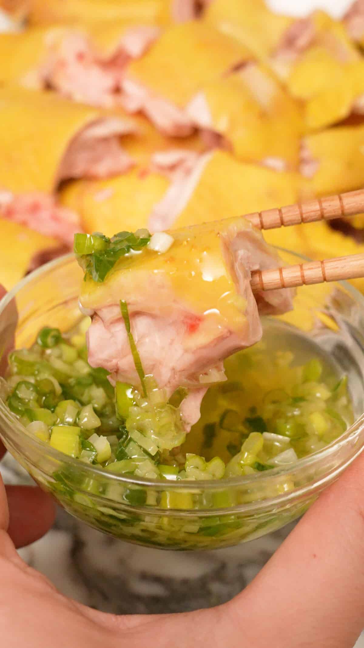 A piece of chicken being dipping in the ginger scallion sauce.