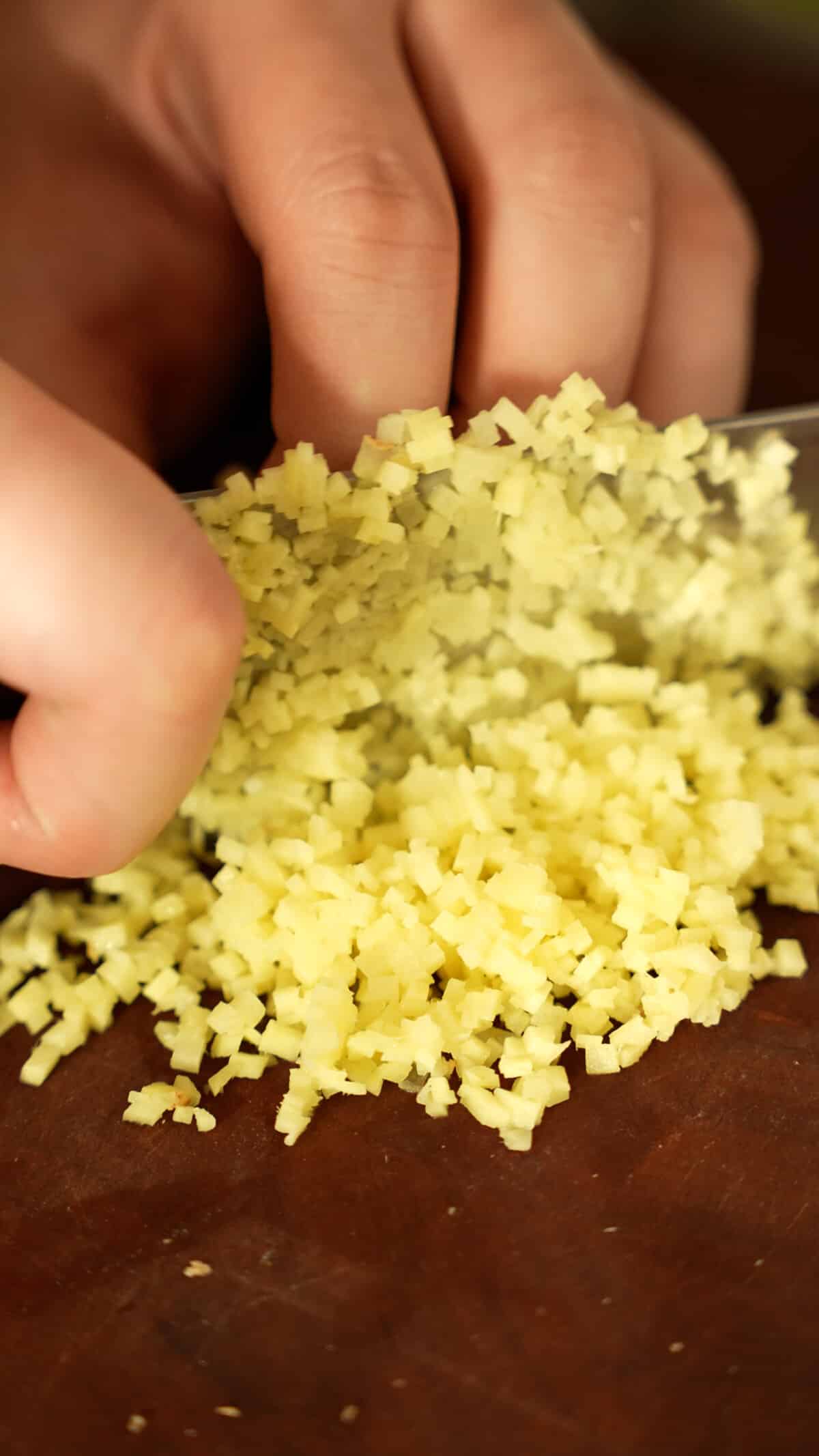 A knife finely mincing ginger on a cutting board.