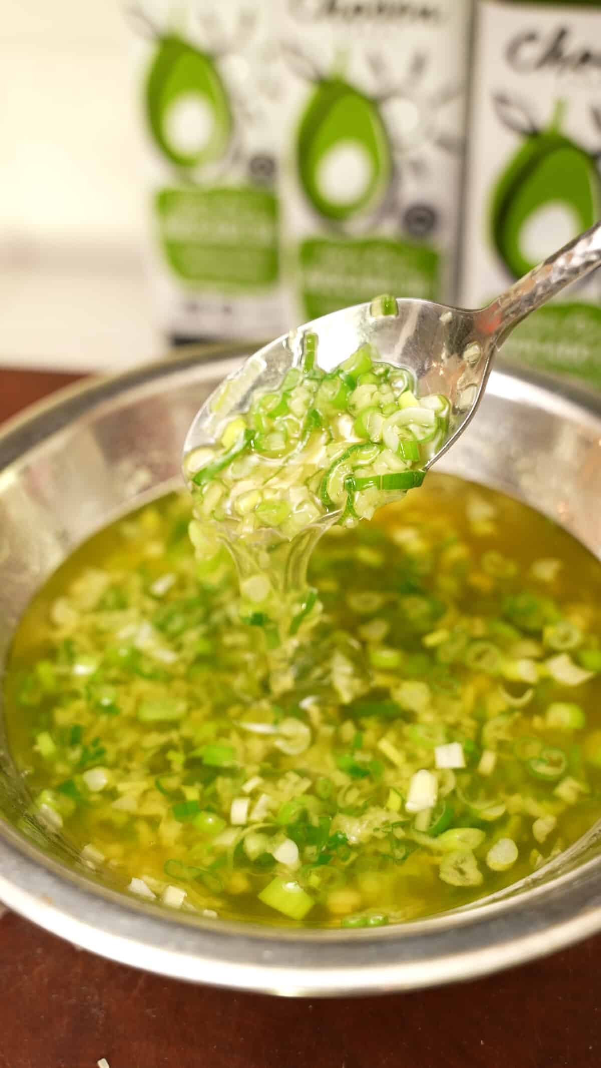 A spoon full of ginger scallion sauce in a metal bowl.