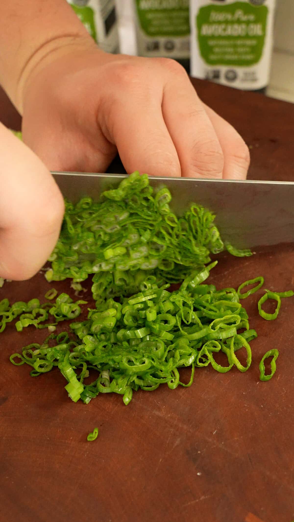 A knife mincing scallion greens on a cutting board.