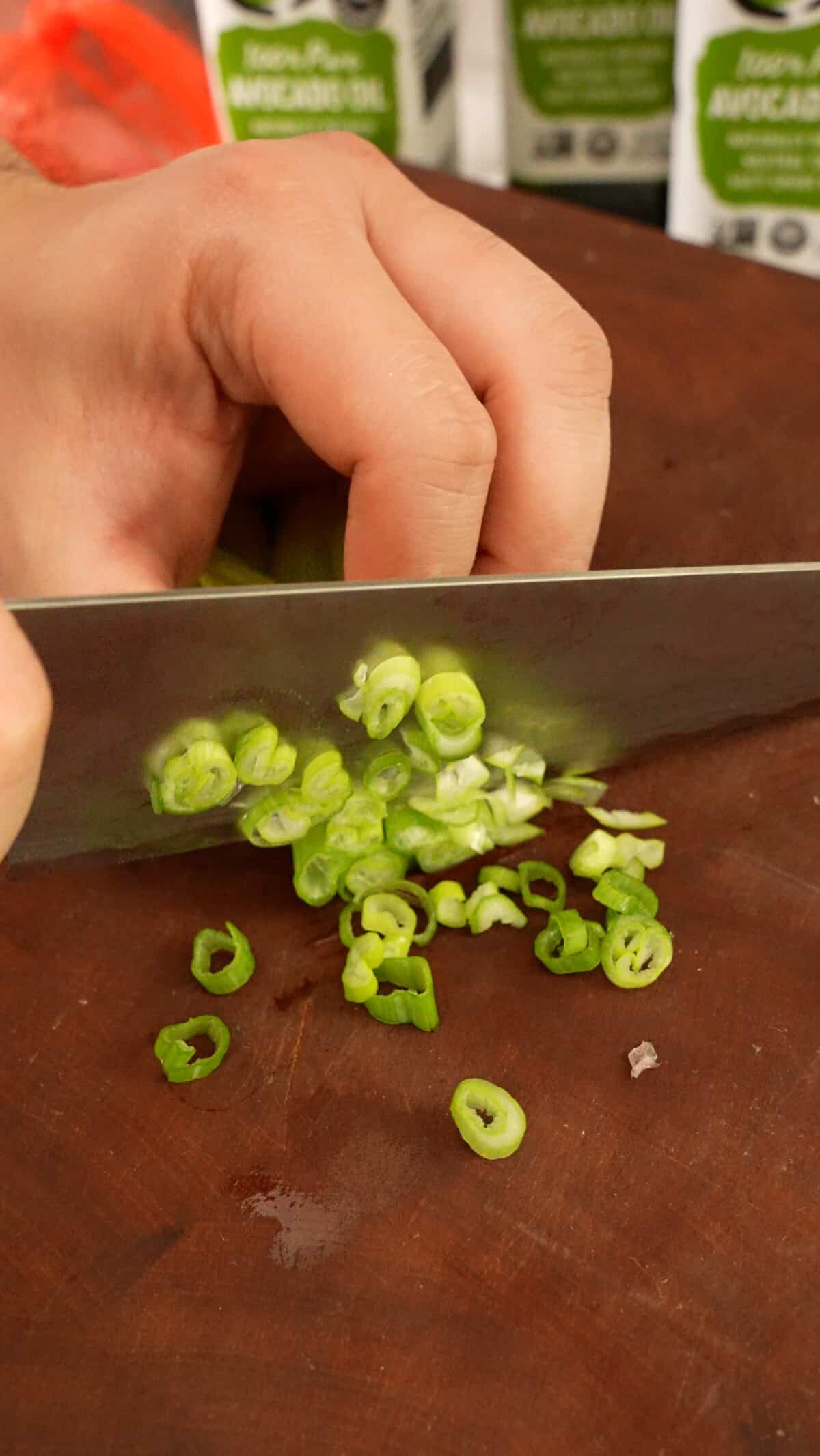 A knife mincing scallion whites on a cutting board.