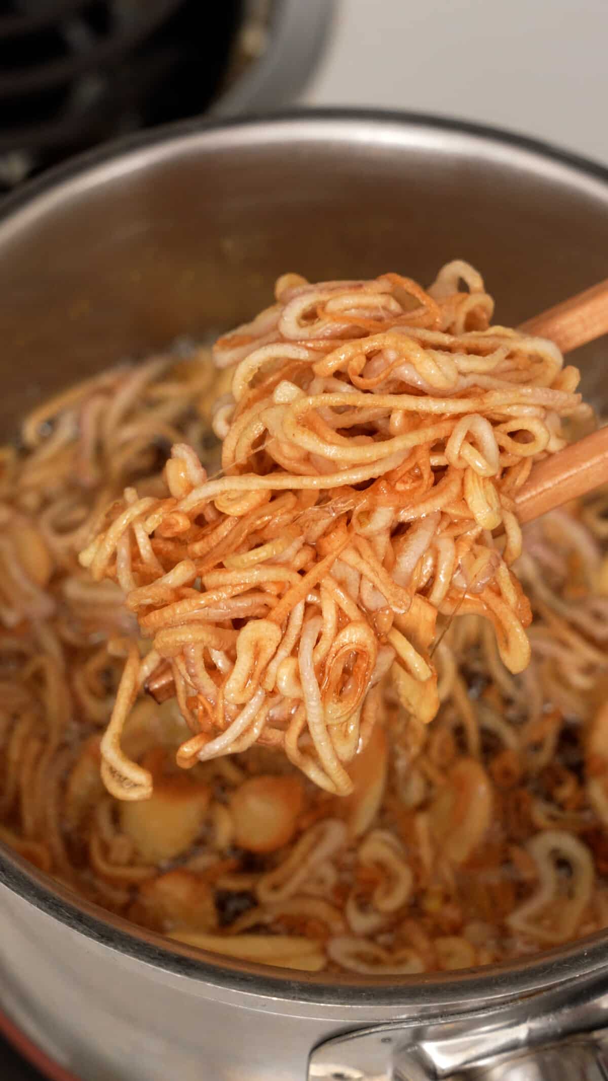 A pair of chopsticks holding up lightly fried shallots and garlic.