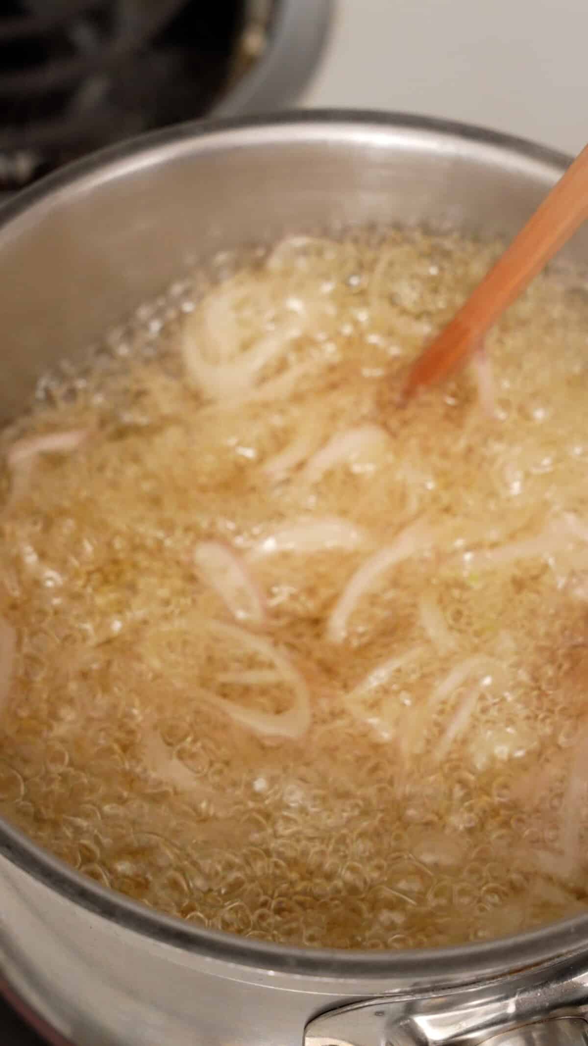 Shallots and garlic frying in a pot of oil.