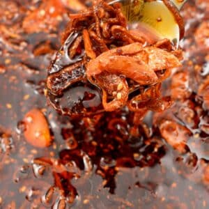 A spoon scooping a spoonful of chili crisp over a larger bowl of the chili crisp.