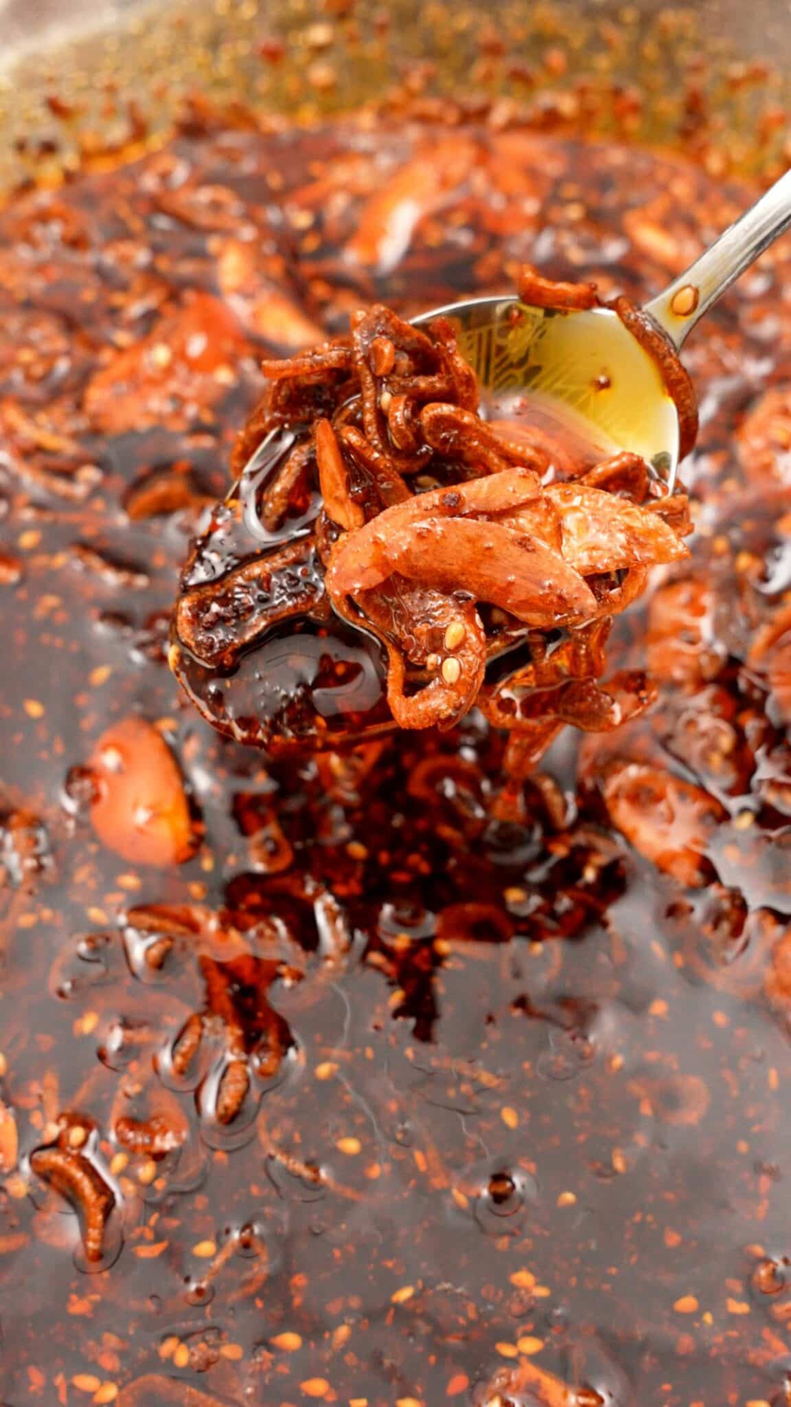 A spoon scooping a spoonful of chili crisp over a larger bowl of the chili crisp.