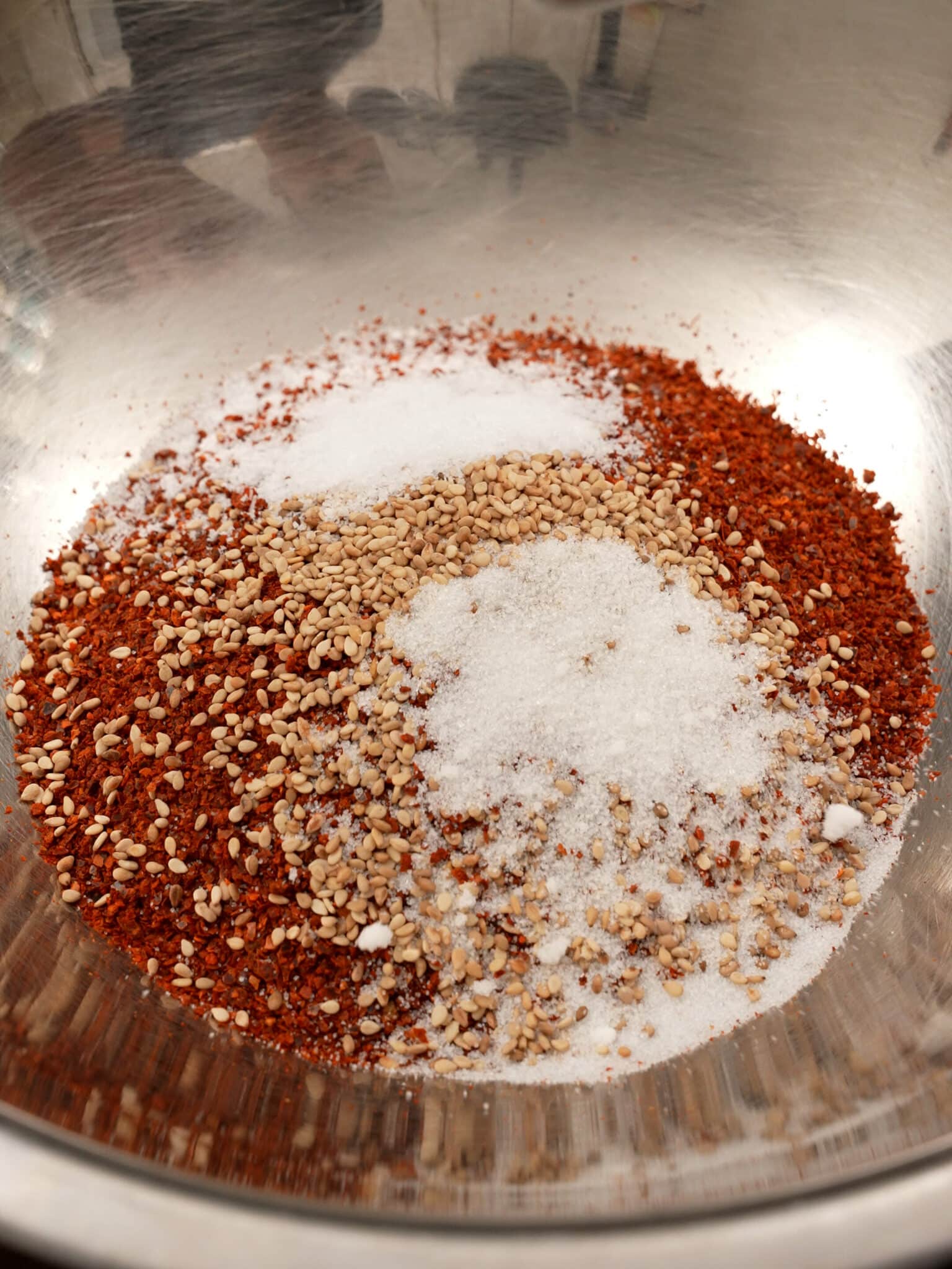 Dry chilies and seasonings being added to a metal bowl.