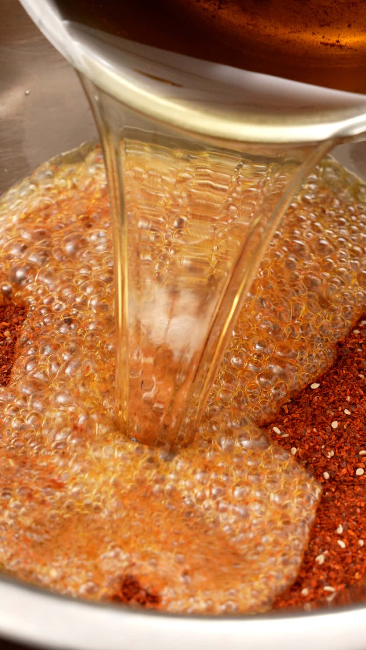 Hot oil being poured onto chilies and seasonings for homemade chili crisp.