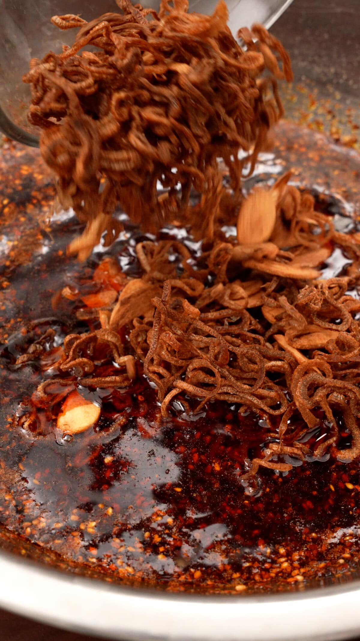 Crispy shallots and garlic being added to the chili oil to make homemade chili crisp.