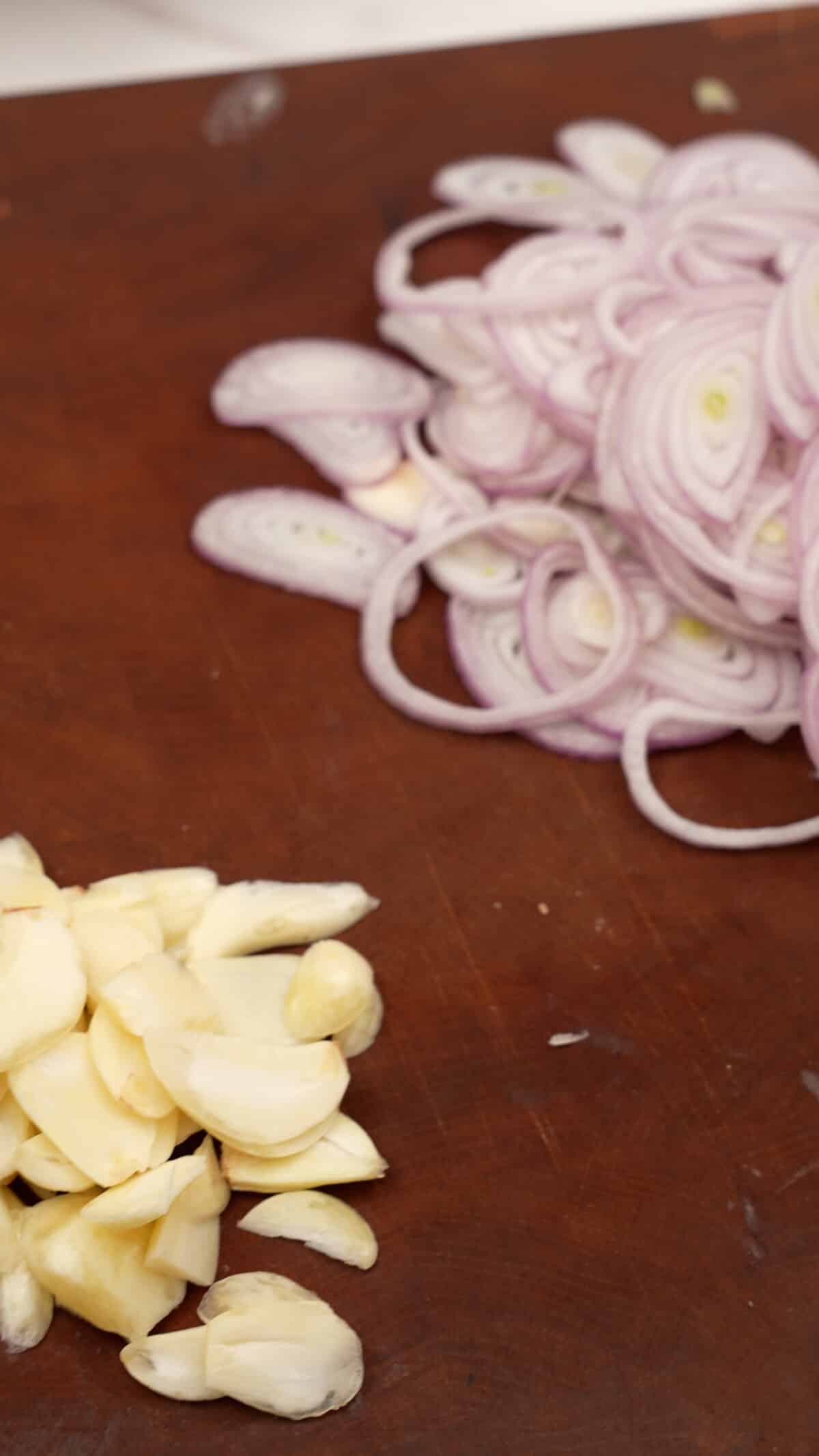 Thinly sliced shallots and garlic on a cutting board.