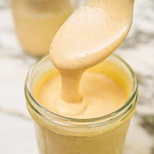 Homemade honey mustard sauce in a glass jar with a spoon.