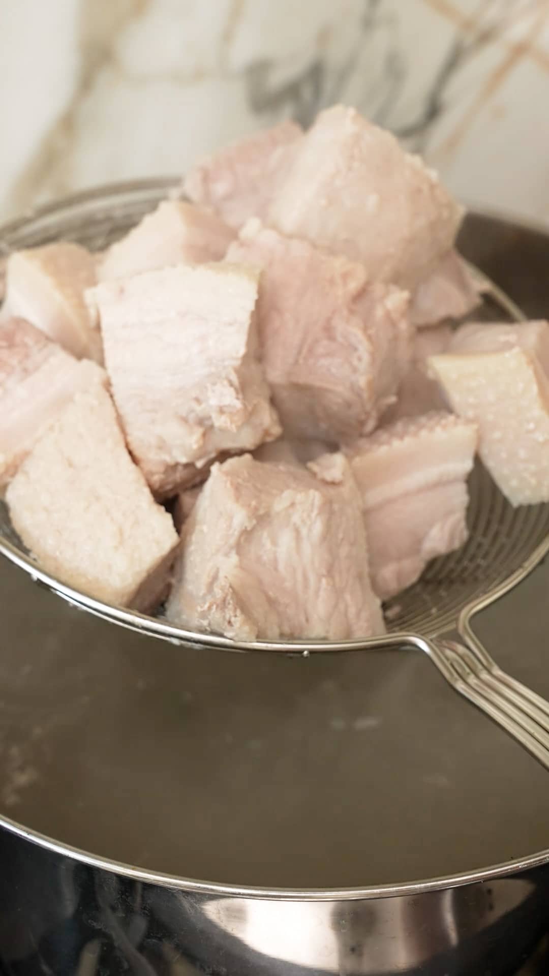 A metal strainer removing blanched pork from the pot.