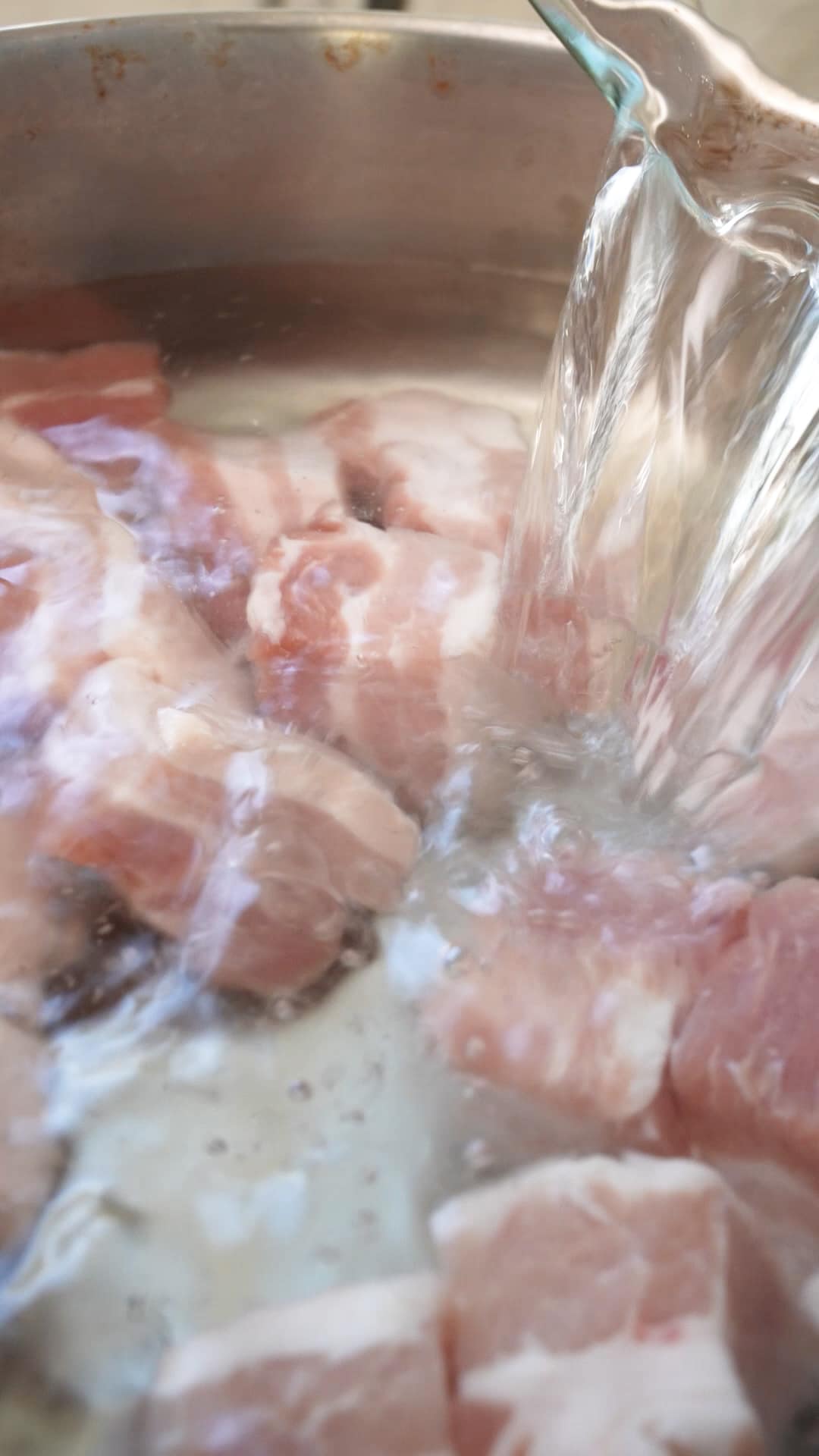 Water being poured over pork belly in a pot.