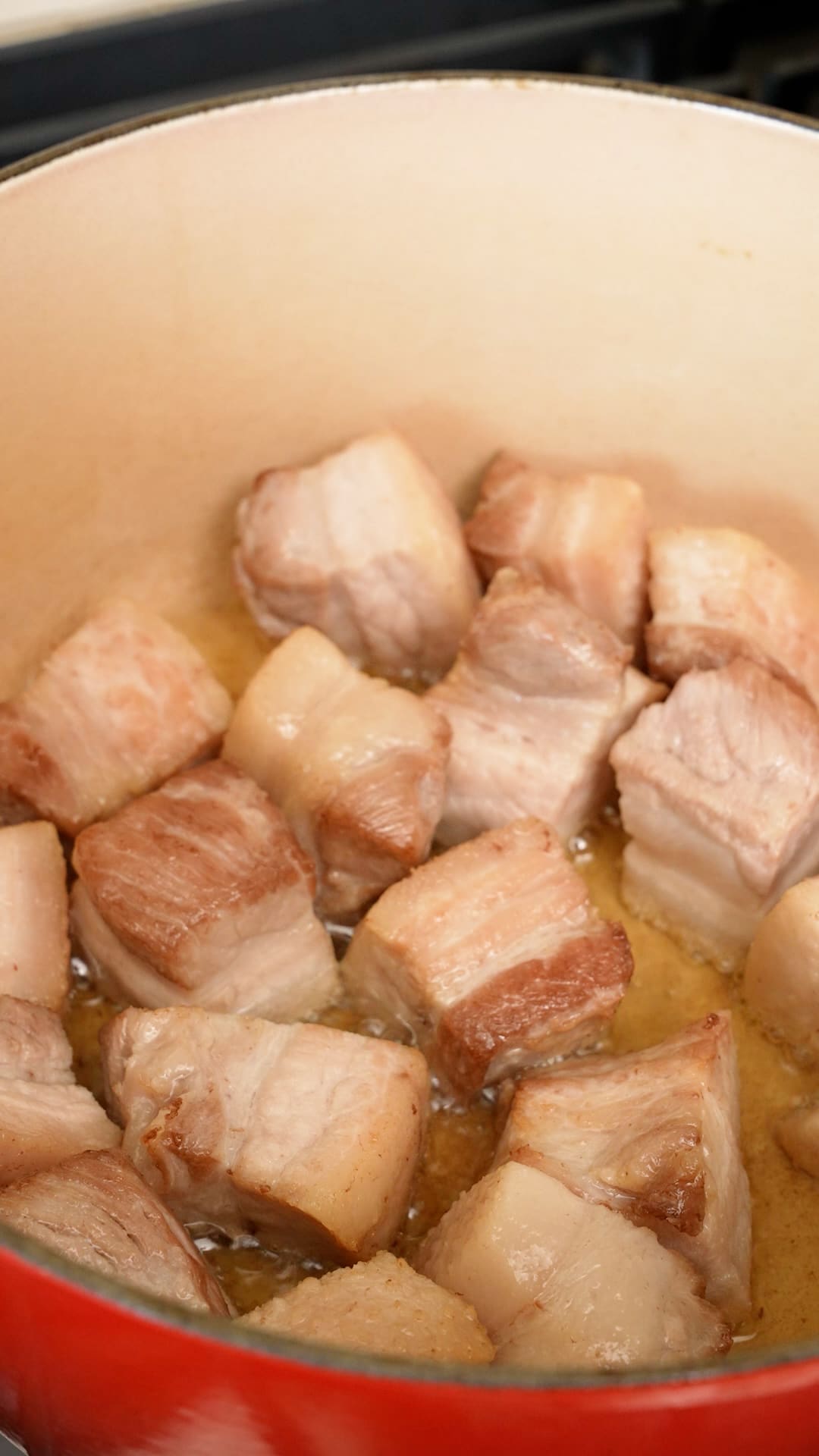 Pork belly frying in a pot with oil.