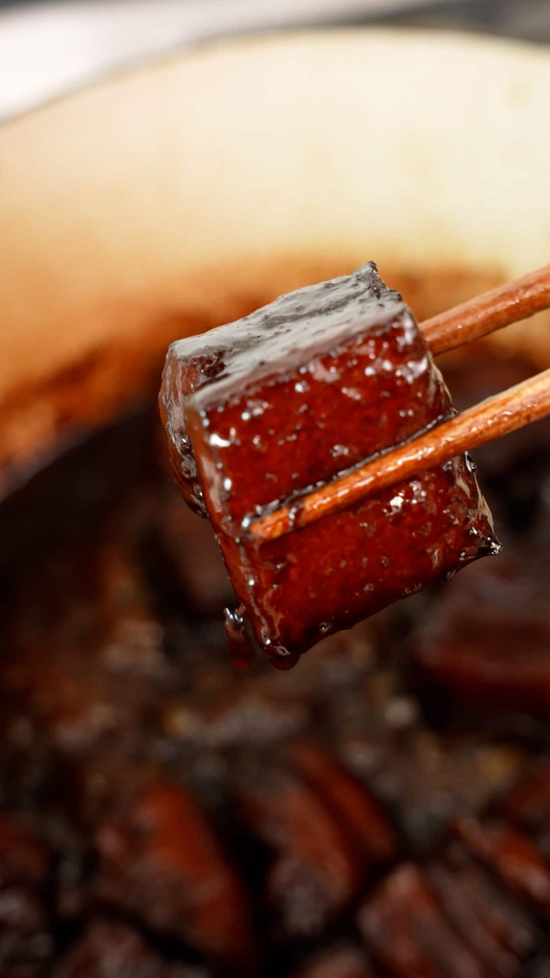 A pair of chopsticks holding up a piece of Hong Shao Rou.