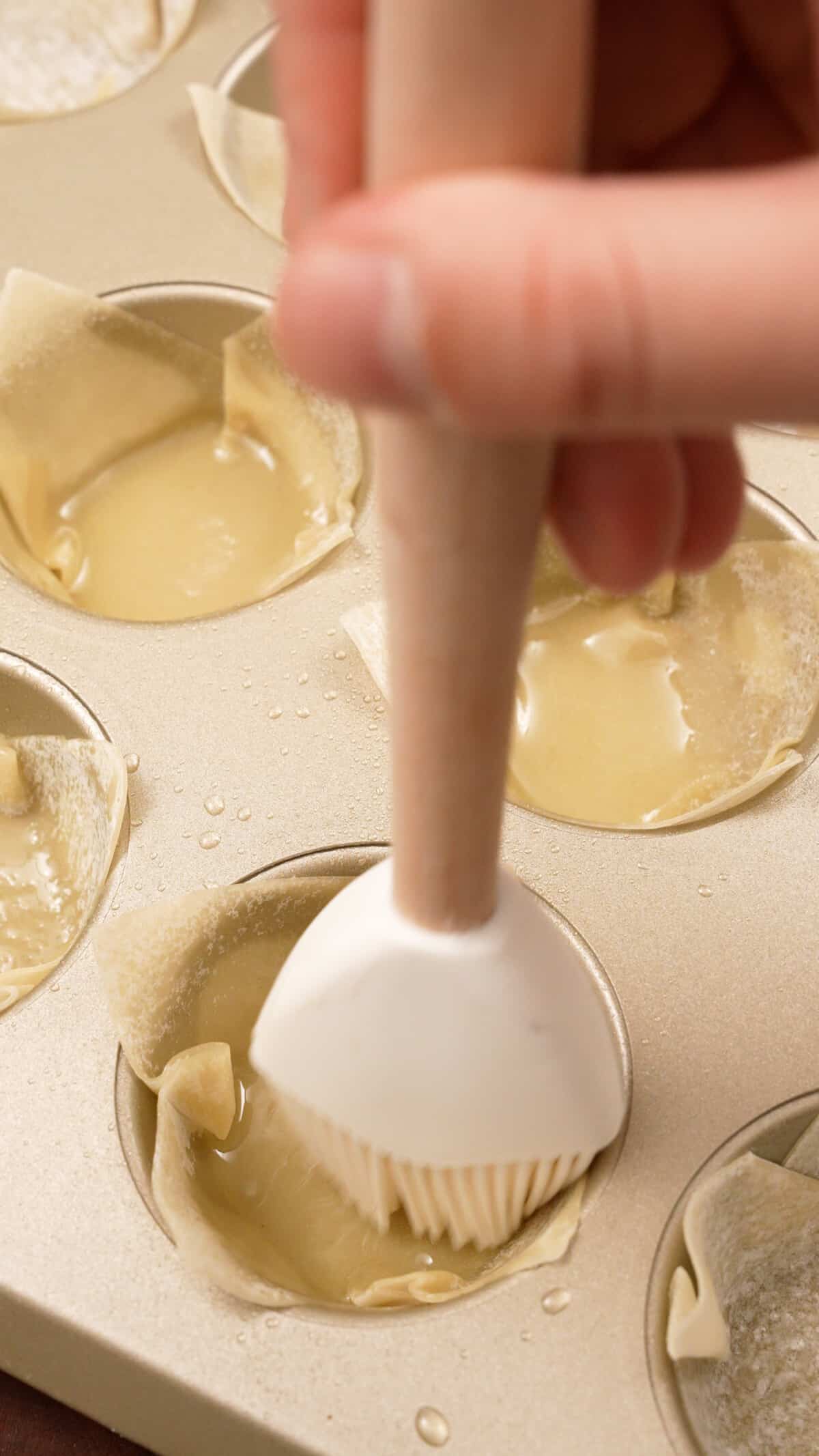 Wonton wrappers being placed in a muffin tin with oil.