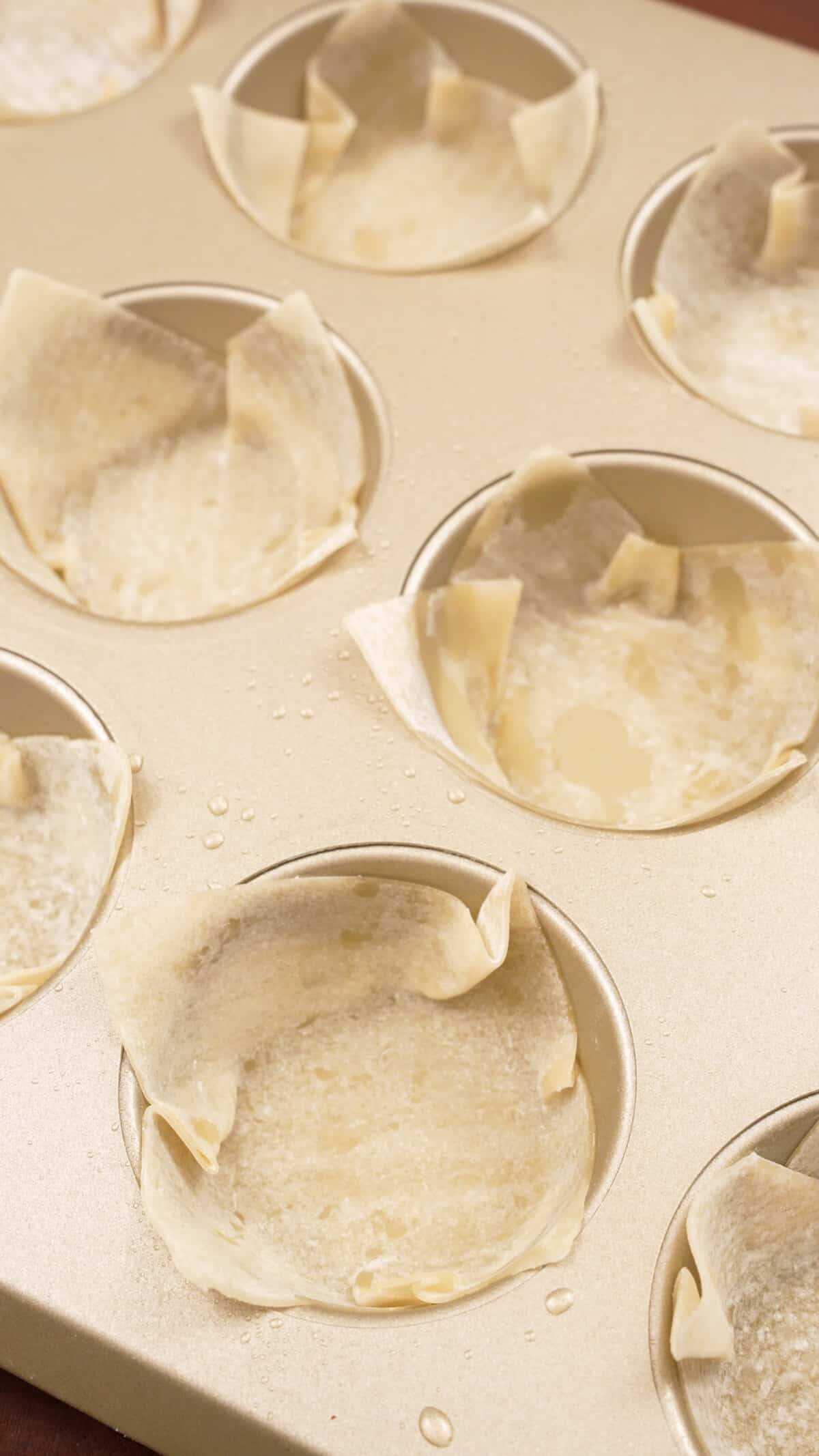 Wonton wrapper skins placed in a muffin tin.