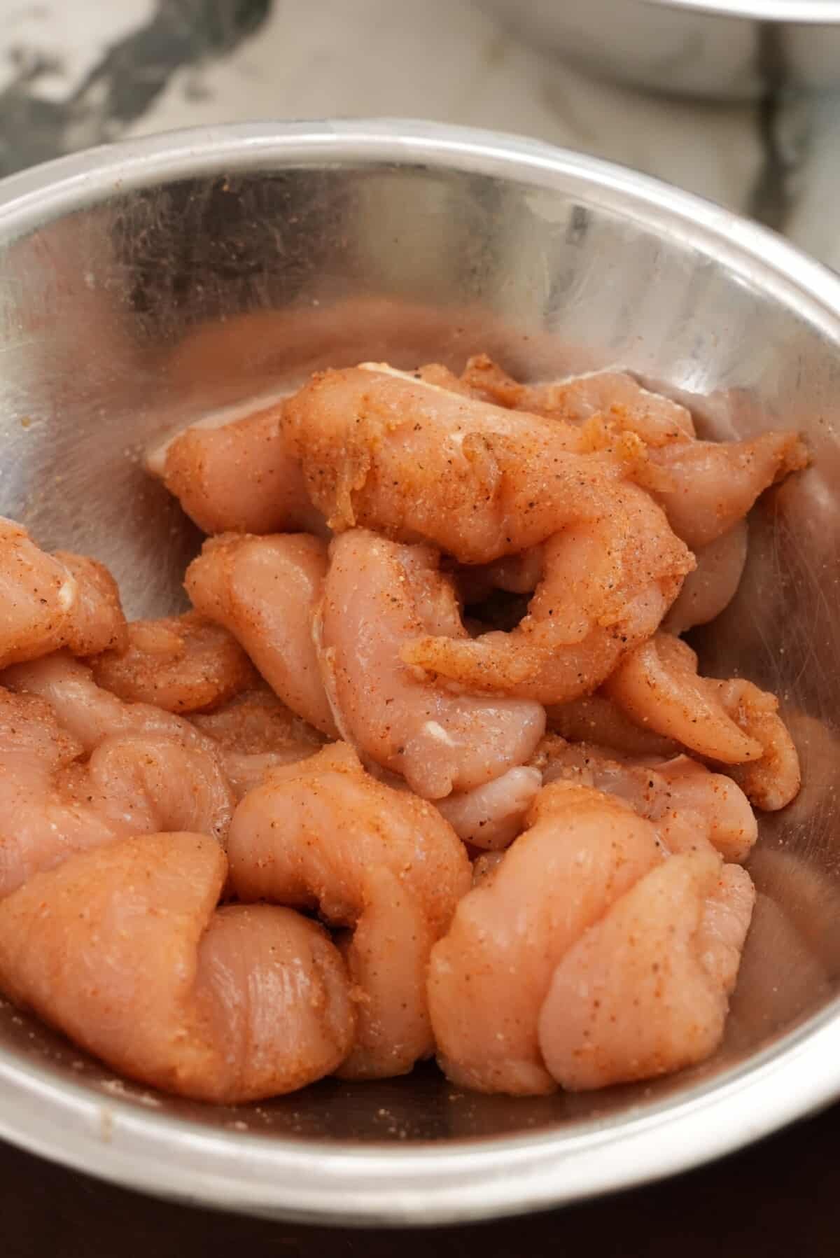 Seasoned chicken in a metal bowl.