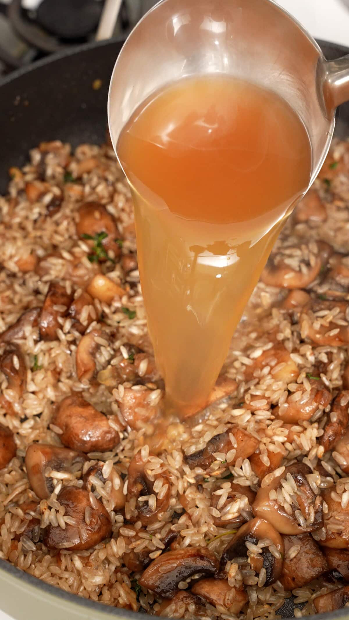 Chicken broth being added to the mushroom risotto in a pan.