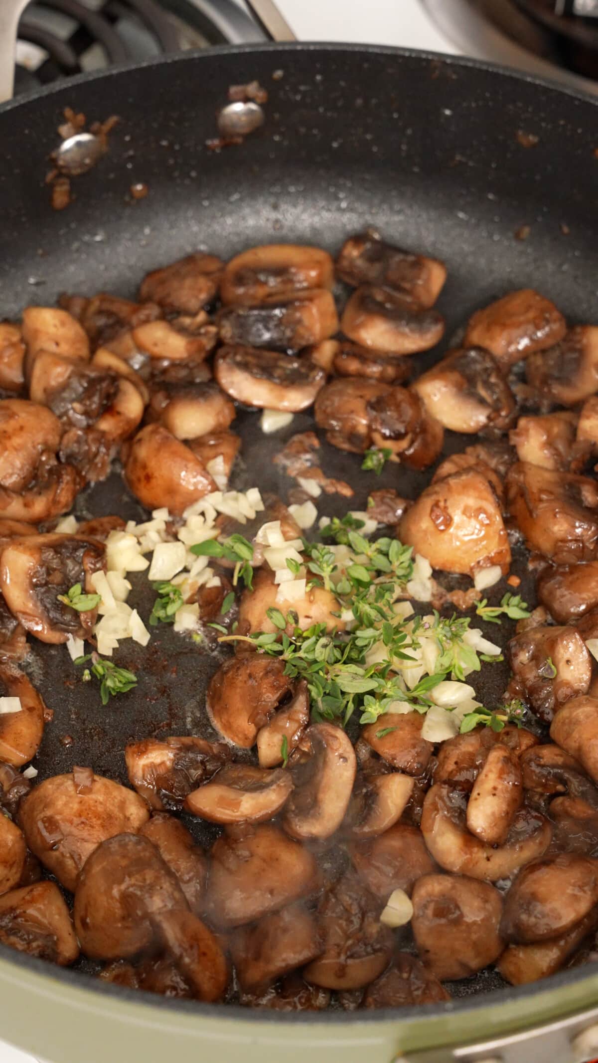 Fresh thyme leaves and fresh garlic being added to a pan with cooked mushrooms.