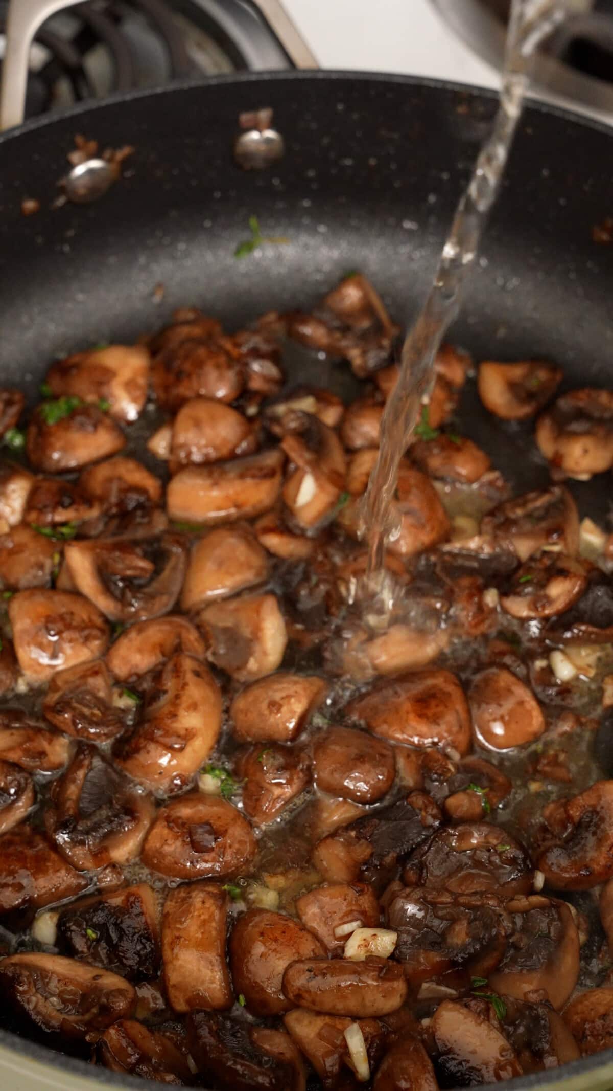 White wine being added to cooked mushrooms in a pan.