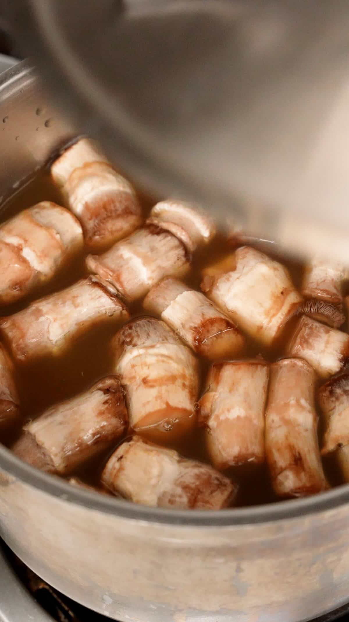 Mushroom stems simmering in chicken broth in a pot.