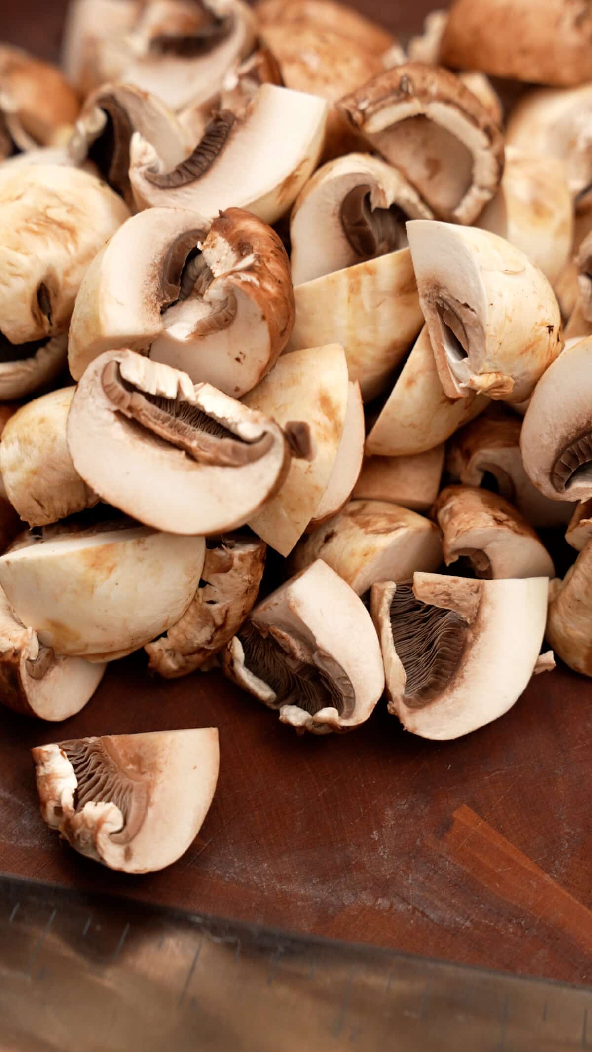 Mushrooms cut into quarters on a cutting board.