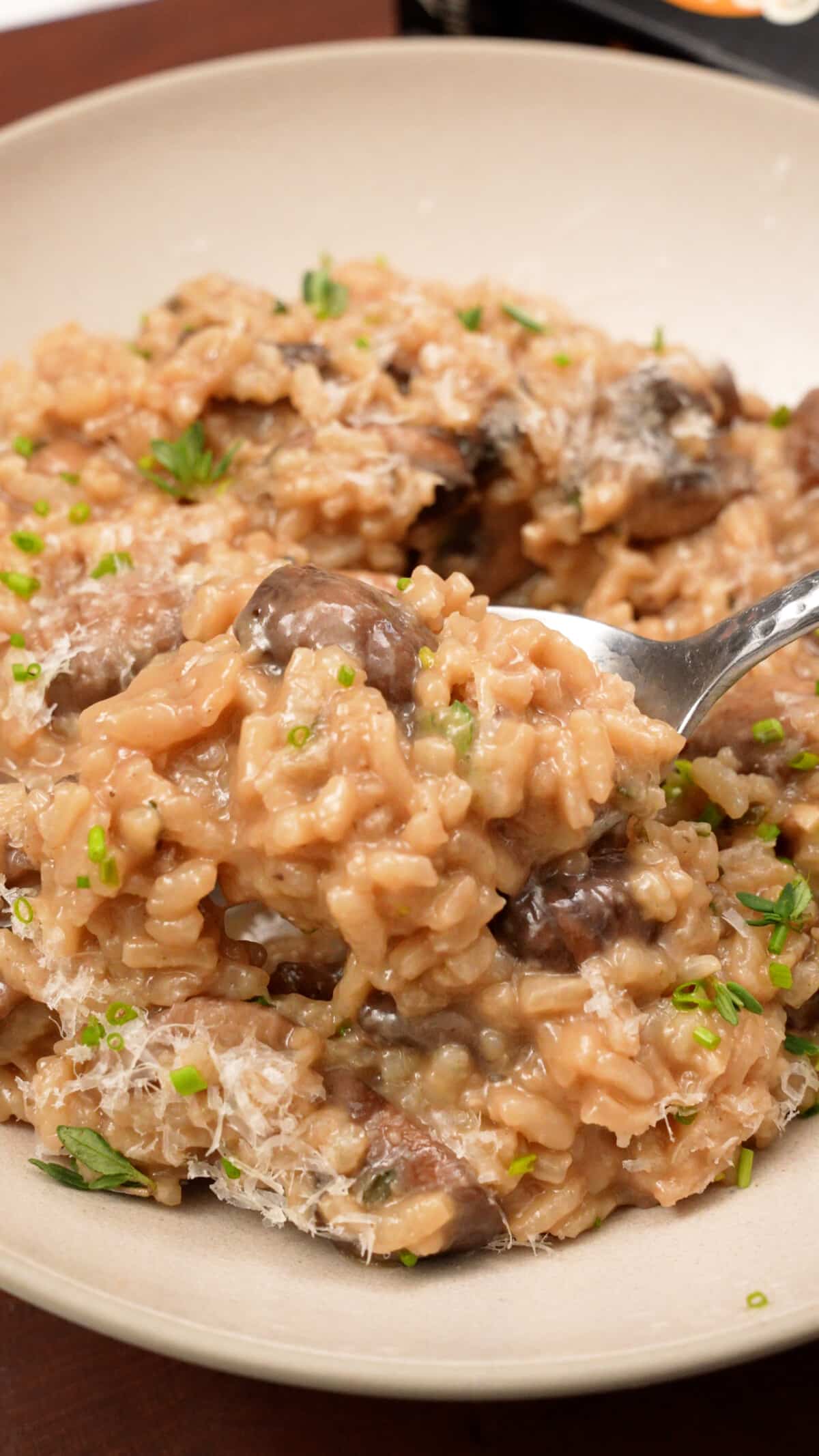 Creamy mushroom risotto being held up with a spoon.