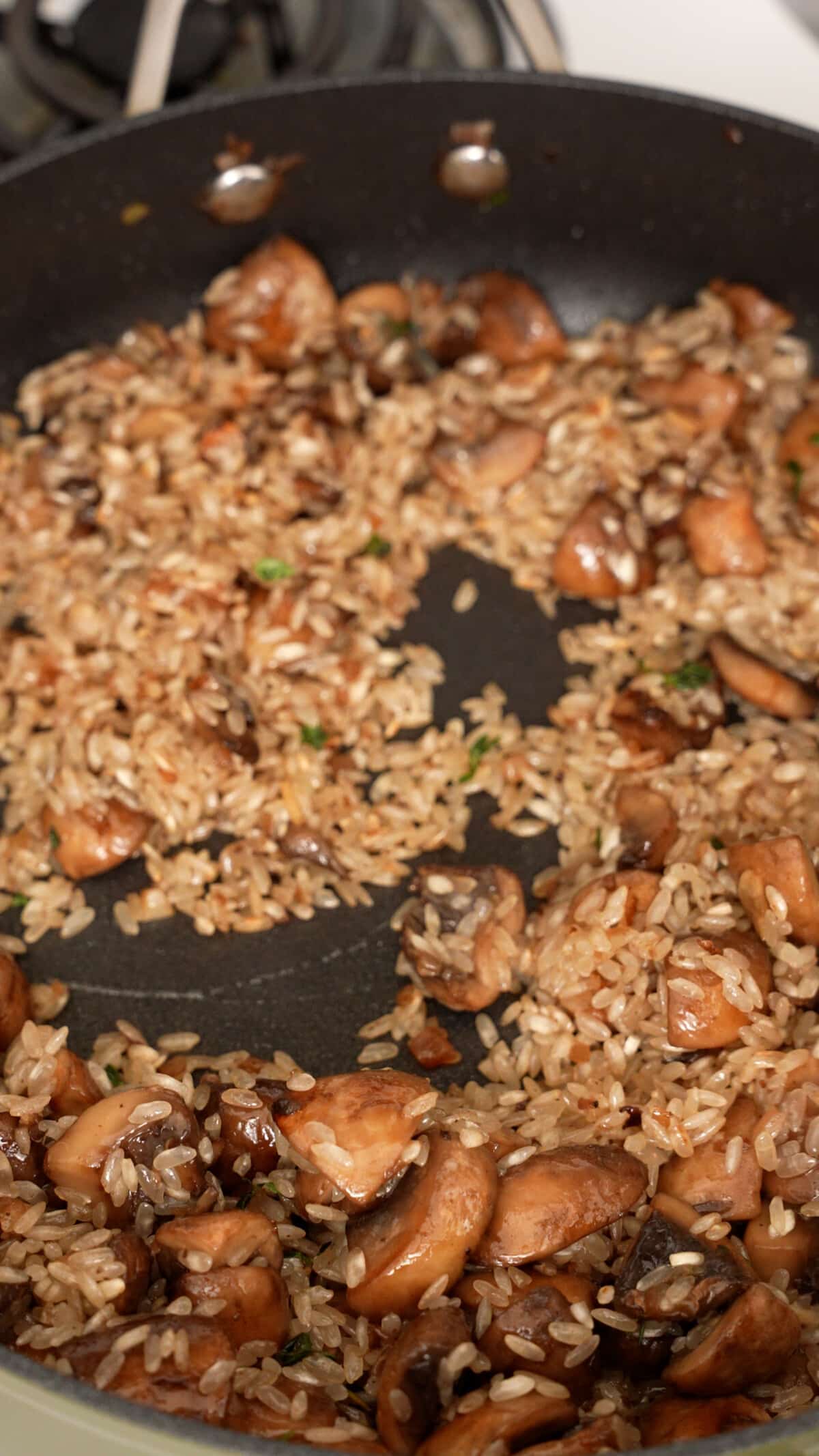 Arborio rice toasting with mushrooms in a pan.