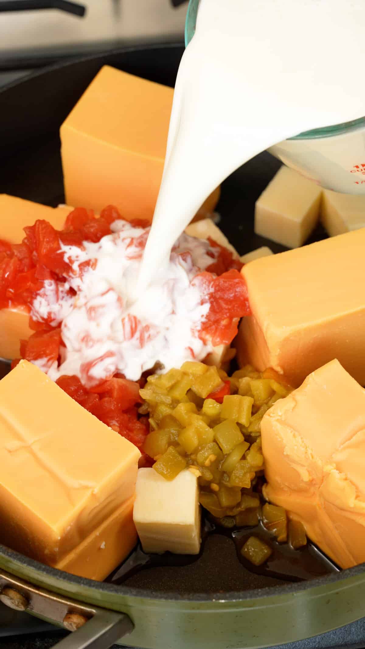 Milk being poured into a pan with velveeta, tomatoes, cheese, and rotel.