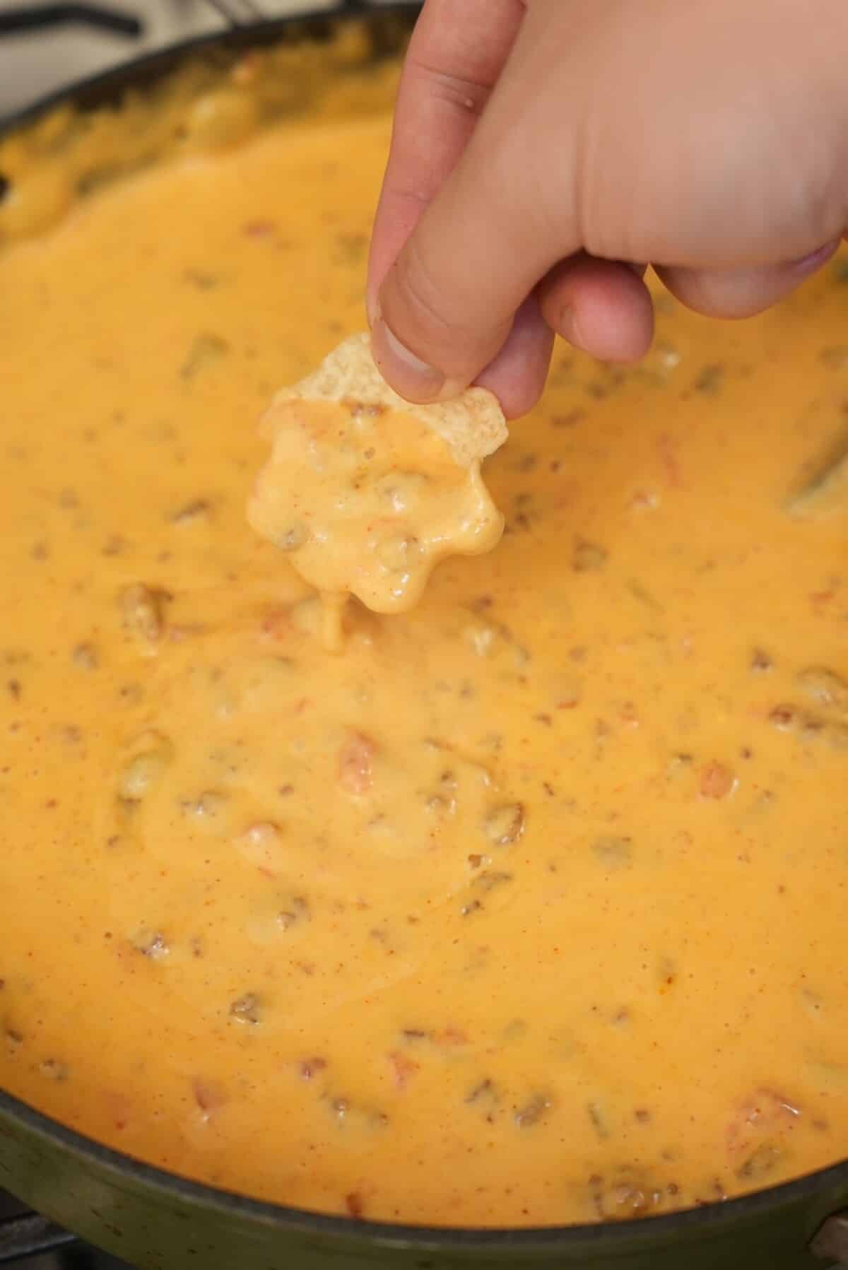 A hand scooping queso dip with a tortilla chip out of the pan.