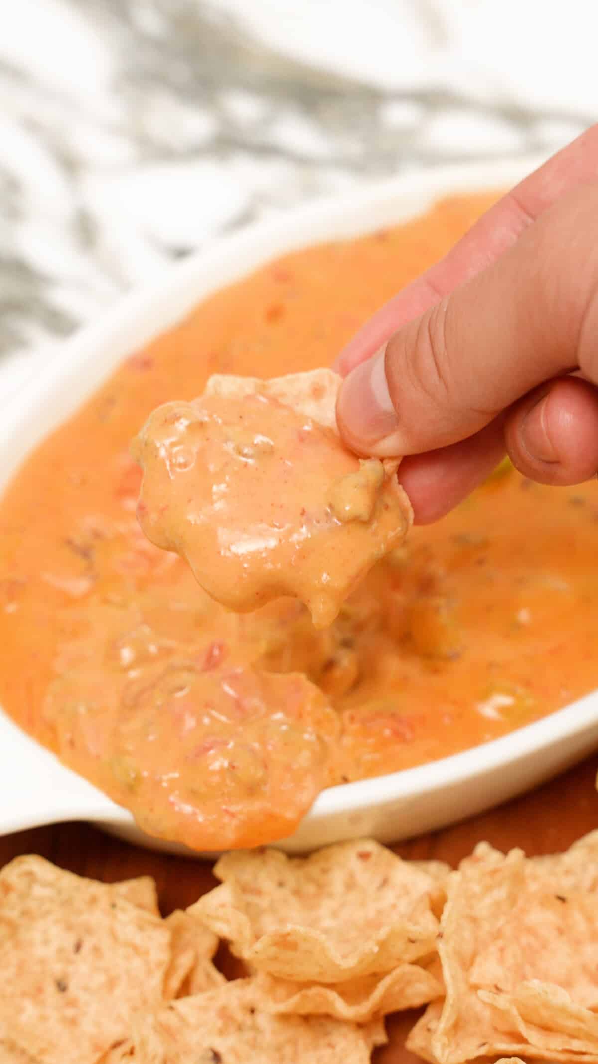 A hand scooping queso dip with a tortilla chip.