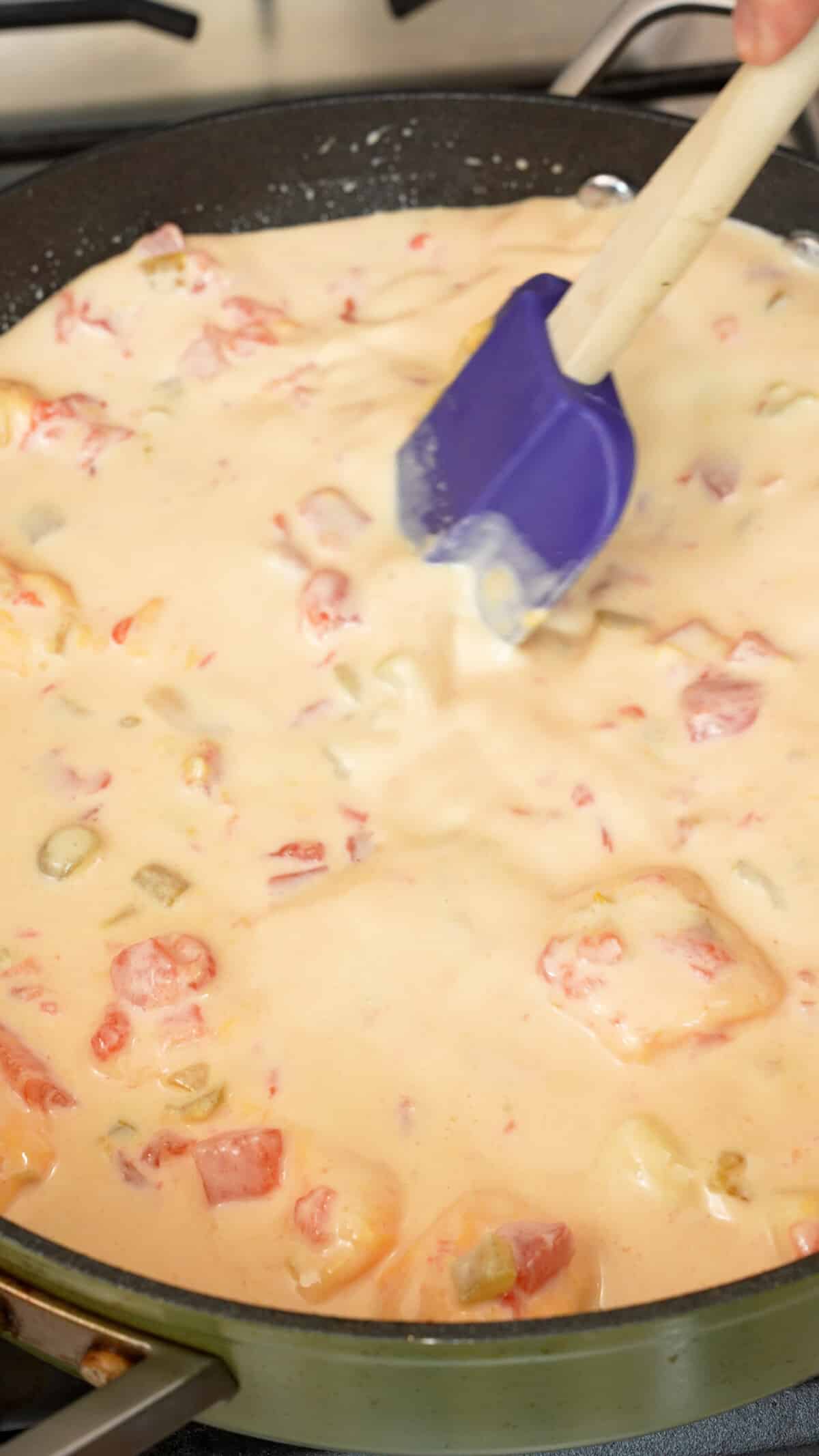 A spatula mixing queso ingredients and milk in a pan.