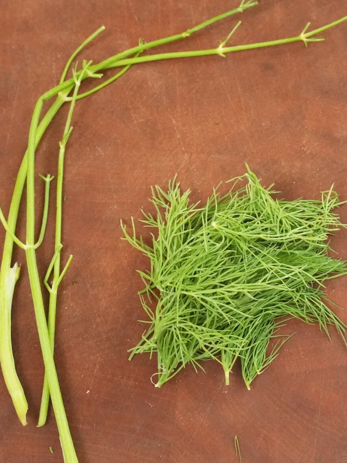 Fresh dill separated from the stems on a cutting board.