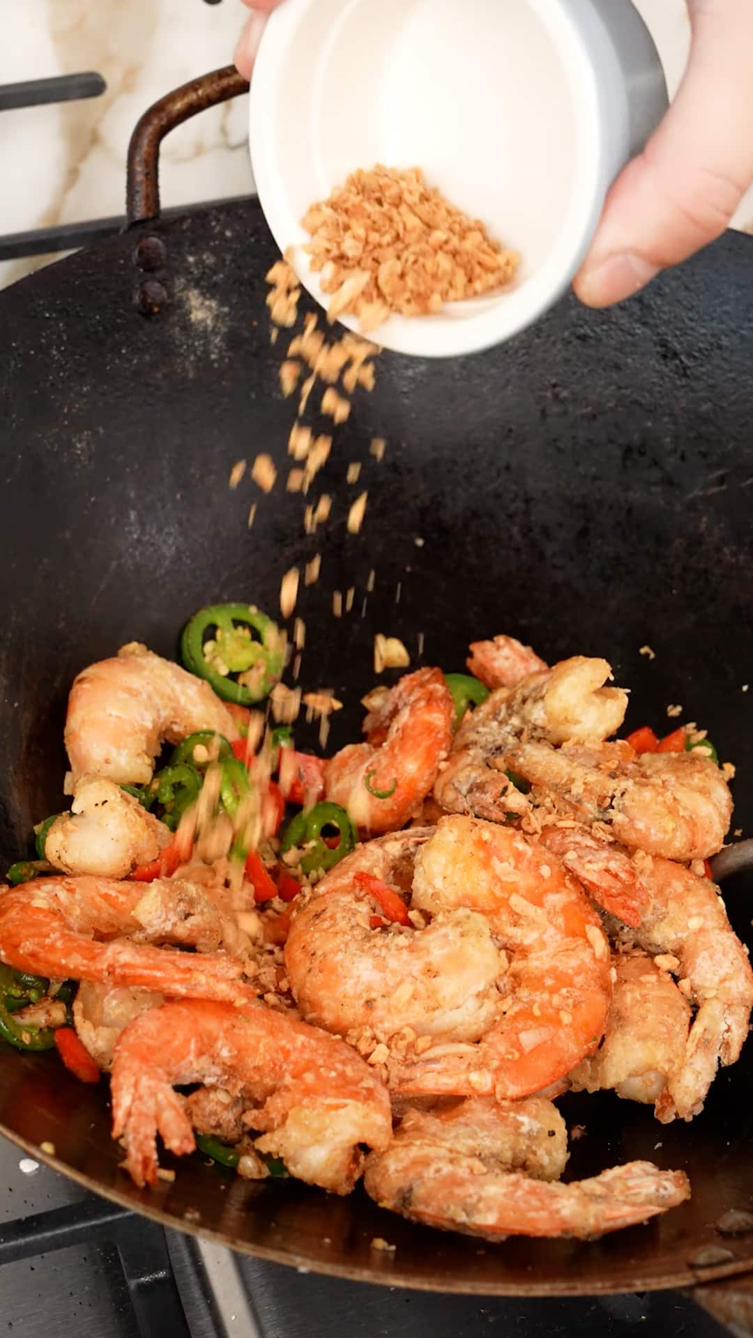 Fried garlic being added onto salt and pepper shrimp in a wok.