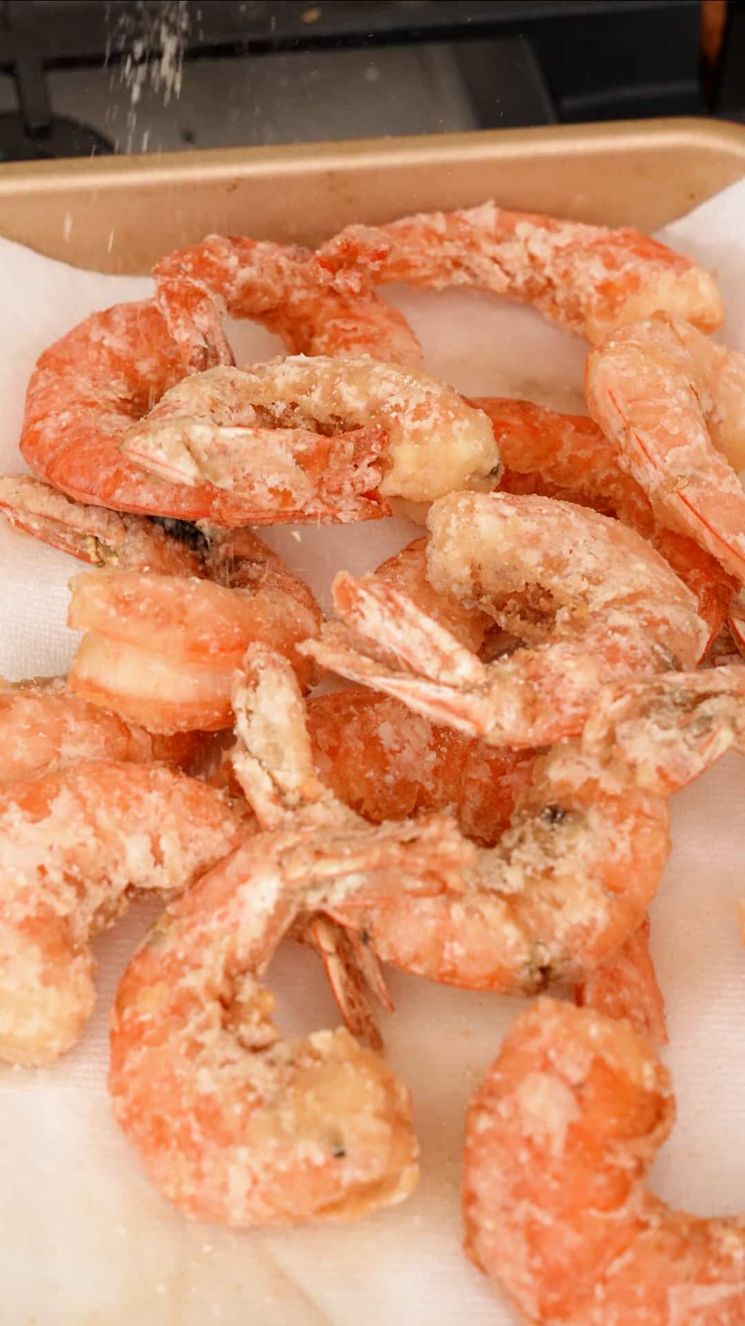Fried shrimp on a tray being coated with spicy salt.