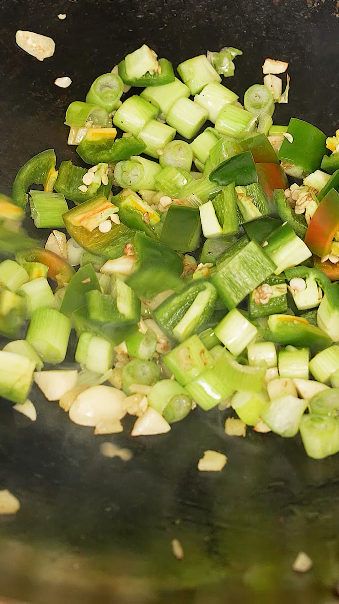 Chopped garlic, peppers, and scallions being stir fried in a wok.