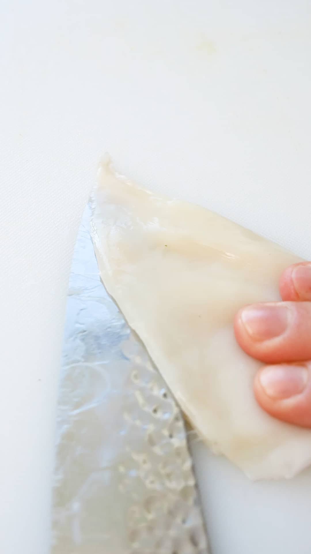 A fresh squid tube being cut in half with a knife.