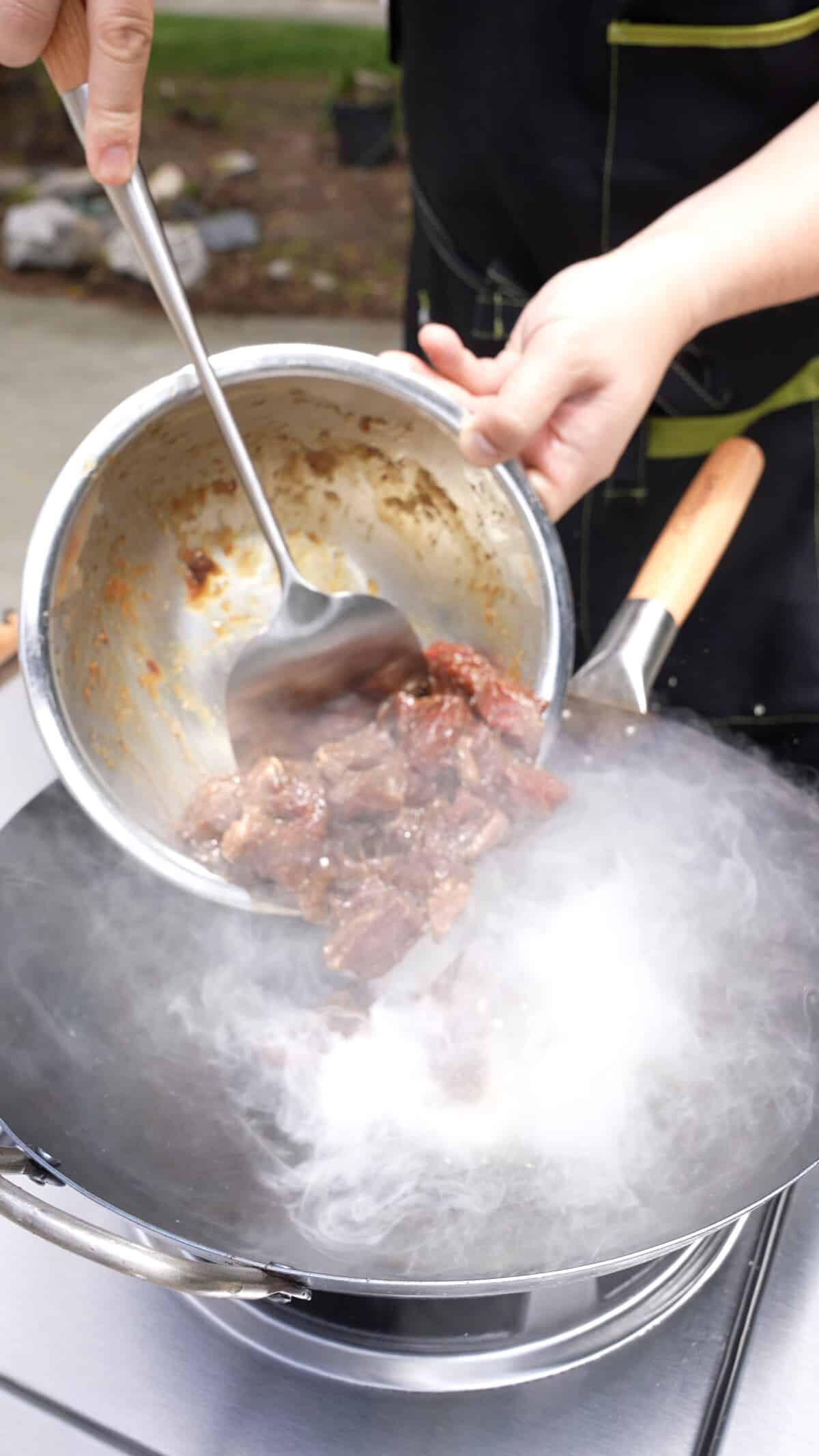 Adding marinated beef to a hot wok.