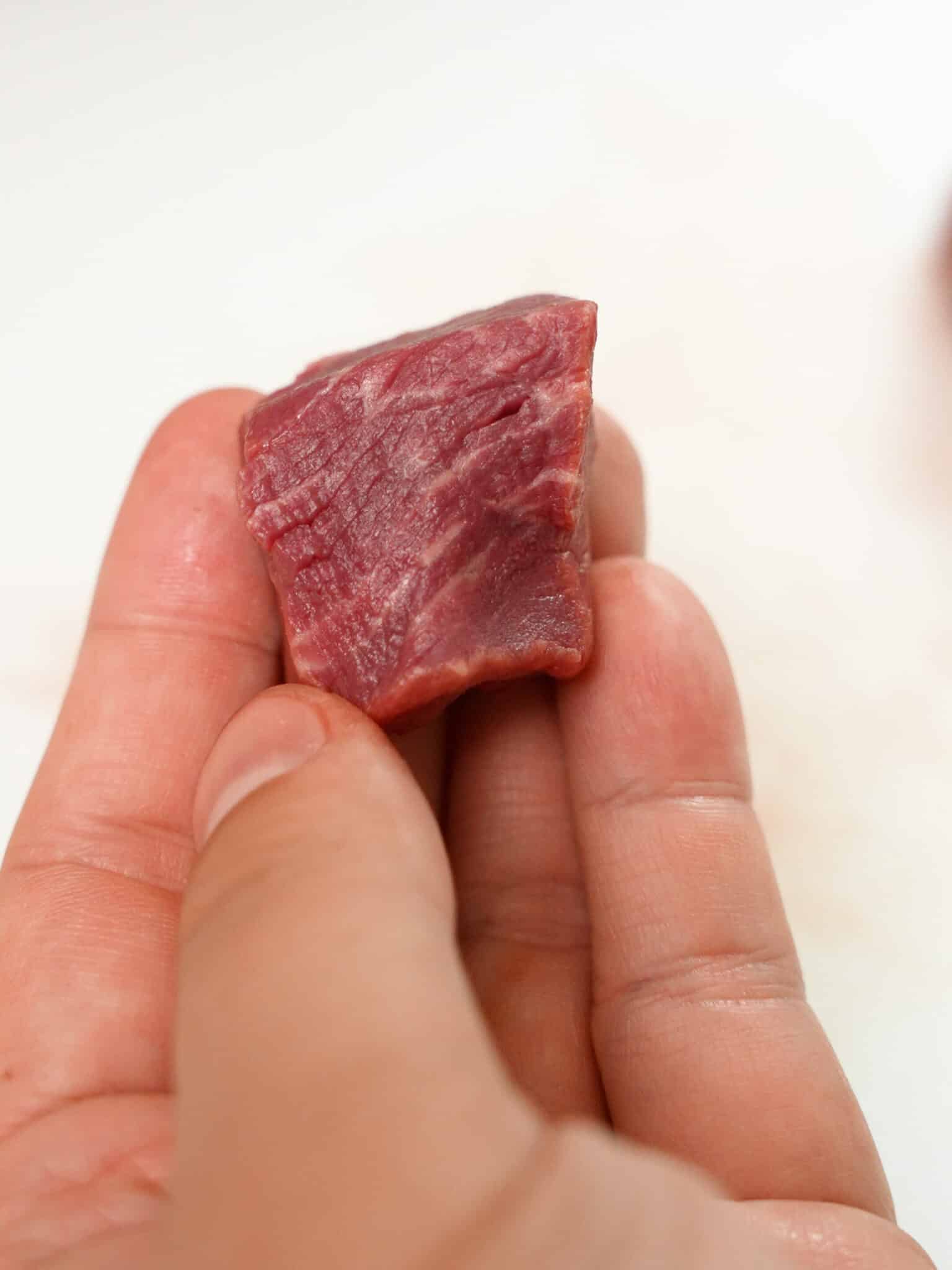 A hand holding a piece of cubed beef.