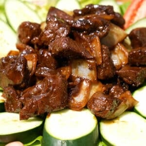 Shaking Beef on a plate with cucumbers and tomatoes.