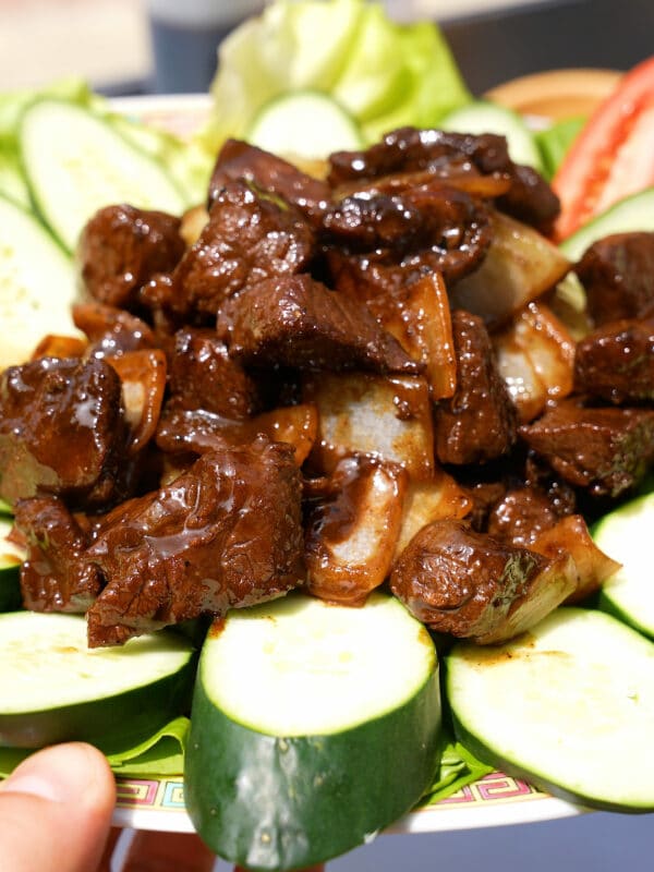 Shaking Beef on a plate with cucumbers and tomatoes.