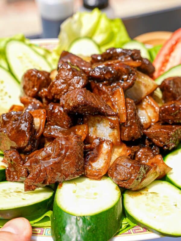 A plate of Shaking Beef (Bo Luc Lac) on a plate with cucumbers and tomatoes.