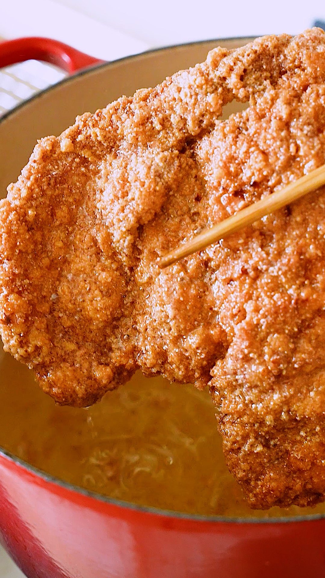 A pair of chopsticks lifting the fried chicken from the oil.