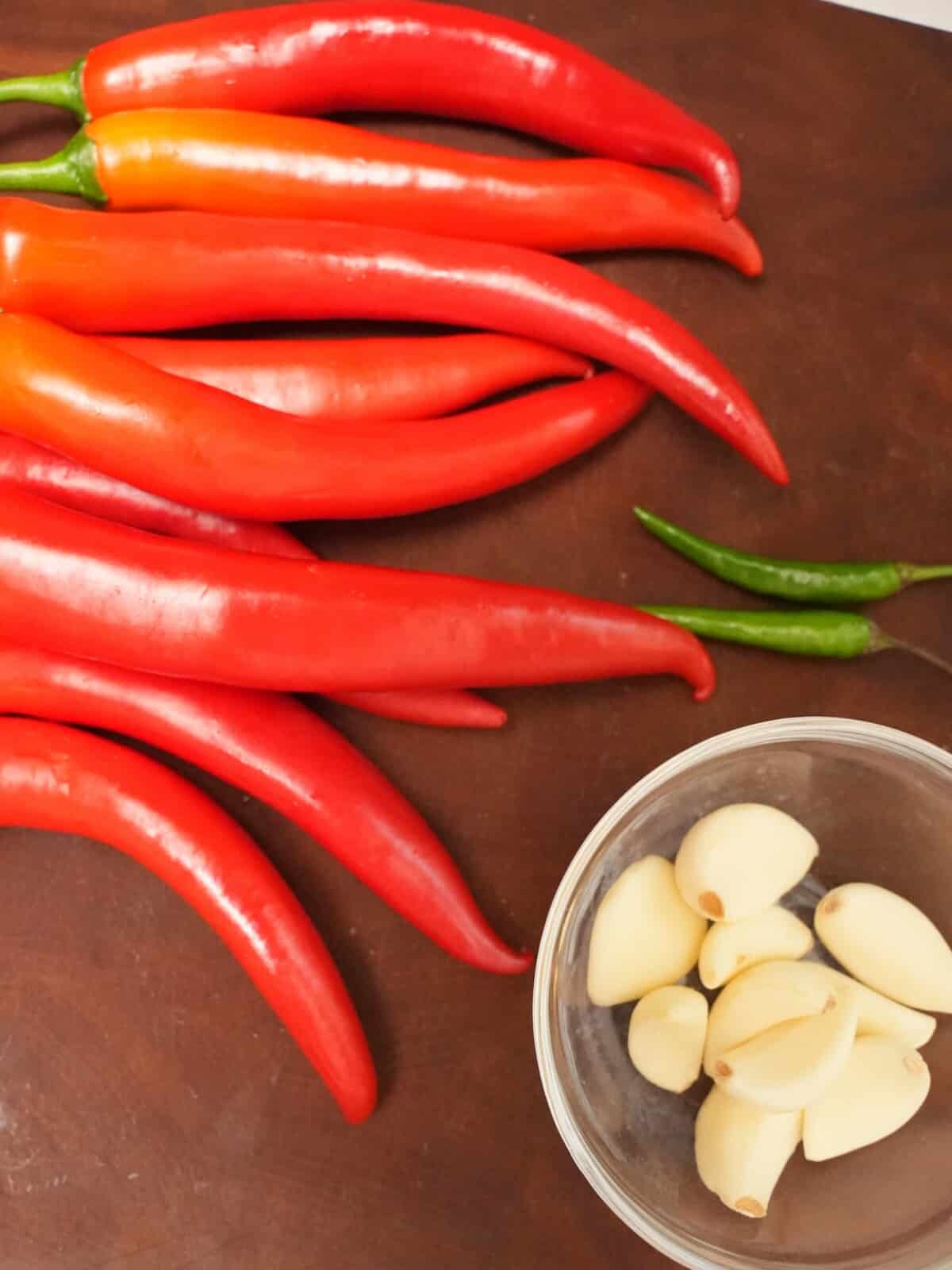 Raw thai chilies and red chilies with garlic on a cutting board.