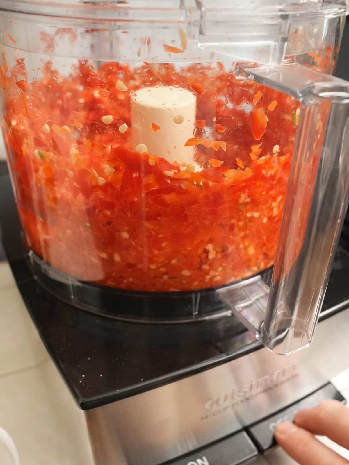 A hand pulsing a food processor blending chilies.